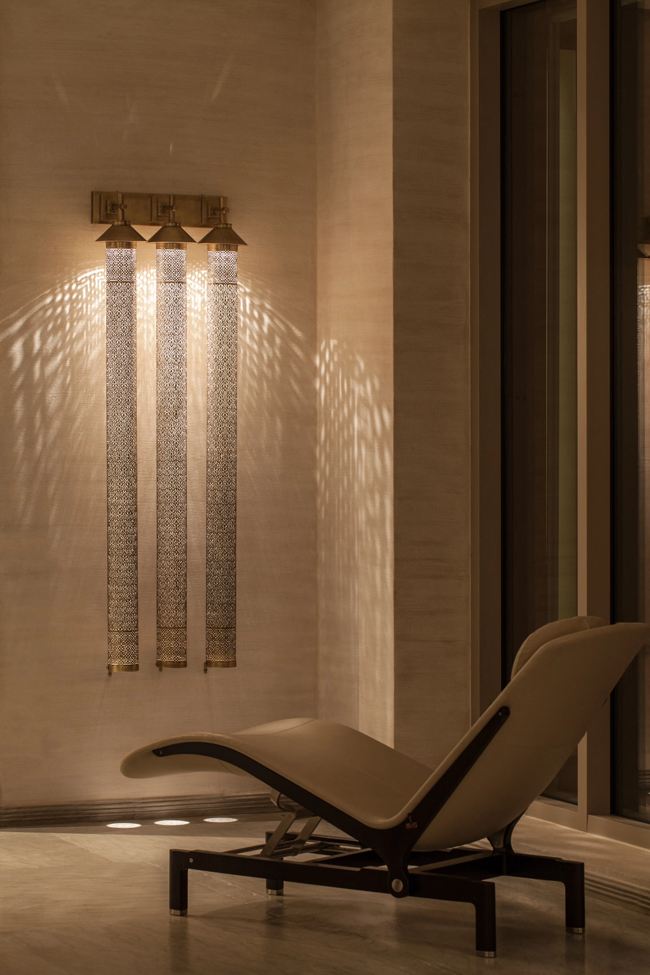 Three tall pierced-cylinder wall lights casting patterns above a single lounge chair.