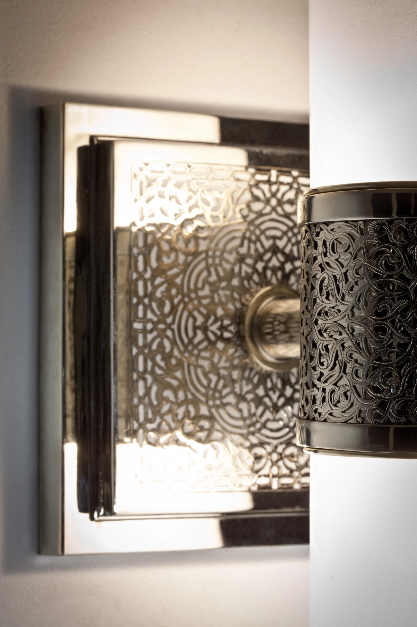 Angled view of a glass-cylinder wall sconce, its pierced enamel backplate glowing behind the frosted tube.