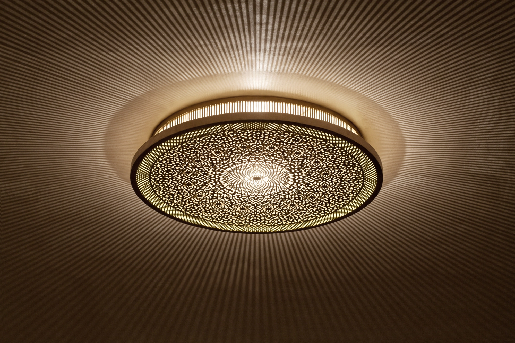 A round pierced metal medallion ceiling light glowing warmly with a soft halo of light around it.