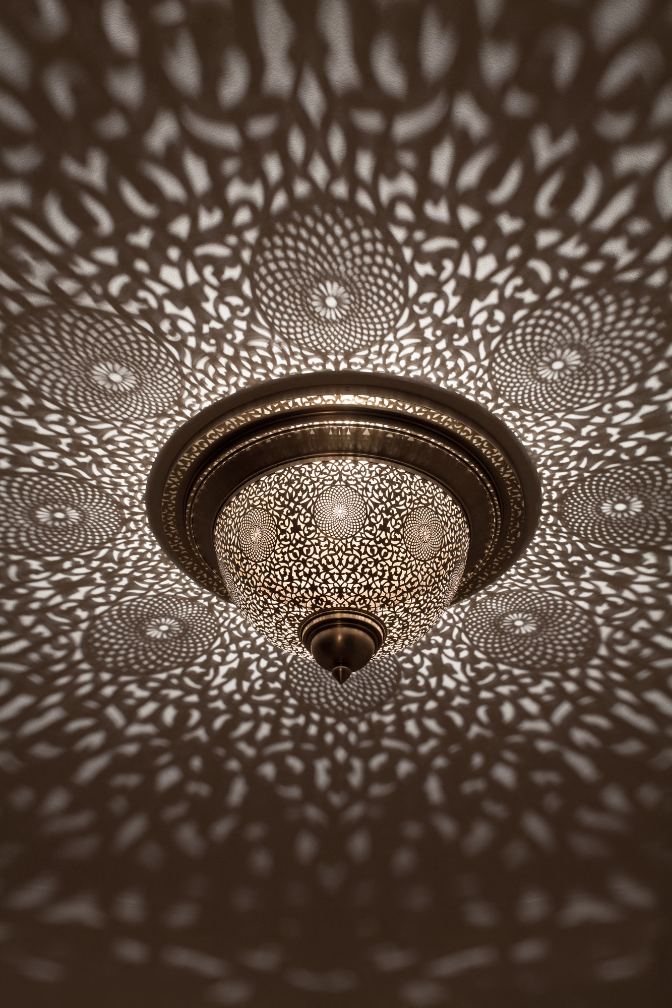A domed pierced metal ceiling light scattering dappled light in a wide circular pattern across the ceiling.