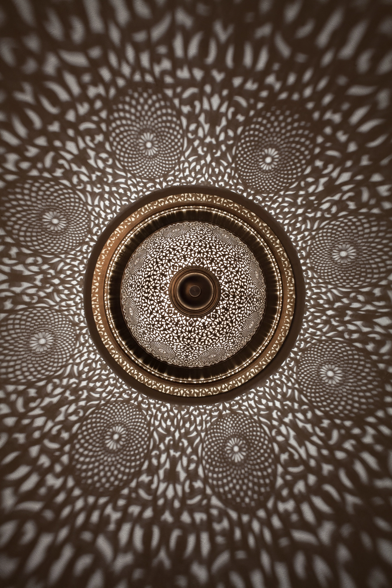 A round pierced ceiling light with concentric rings, casting a dense pattern of dappled light across the ceiling.