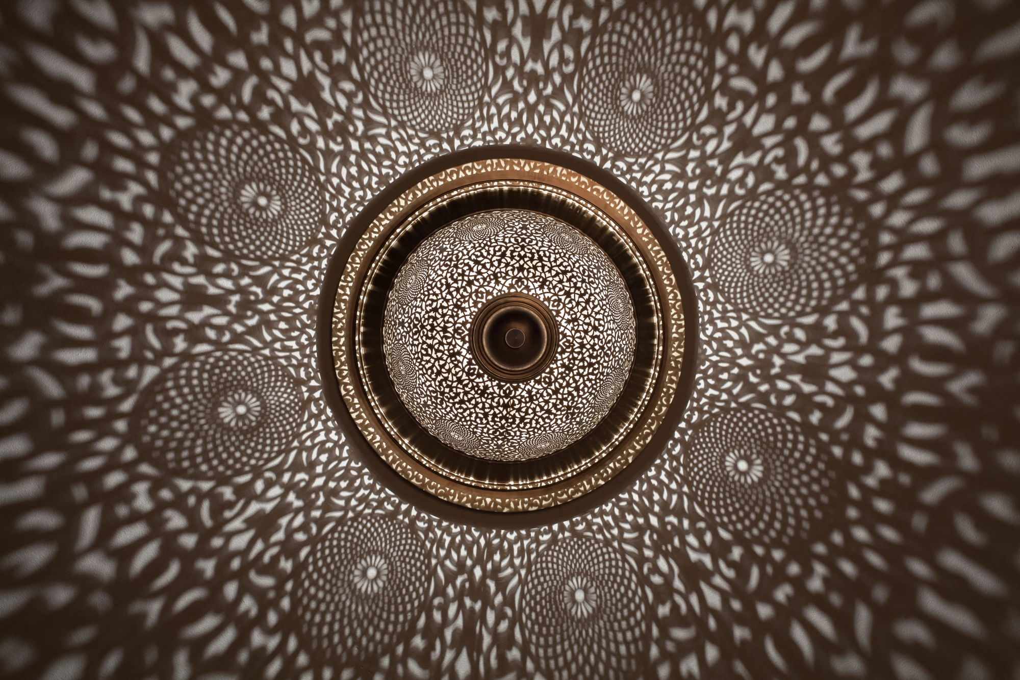 A circular pierced metal ceiling light with concentric bands, scattering dappled light over the ceiling.