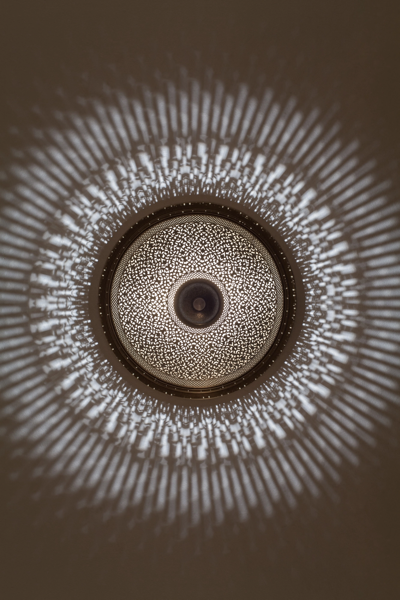 A circular pierced ceiling light casting a radial pattern of dappled light across the ceiling.