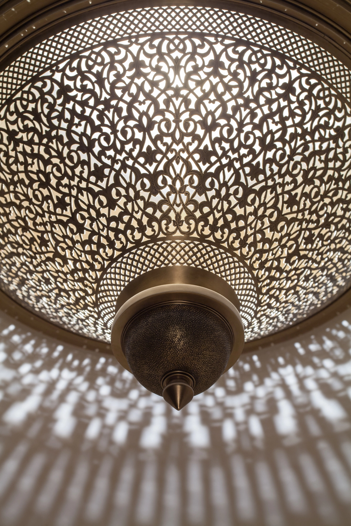 A domed pierced metal ceiling light glowing through dense perforations, viewed close up from below.