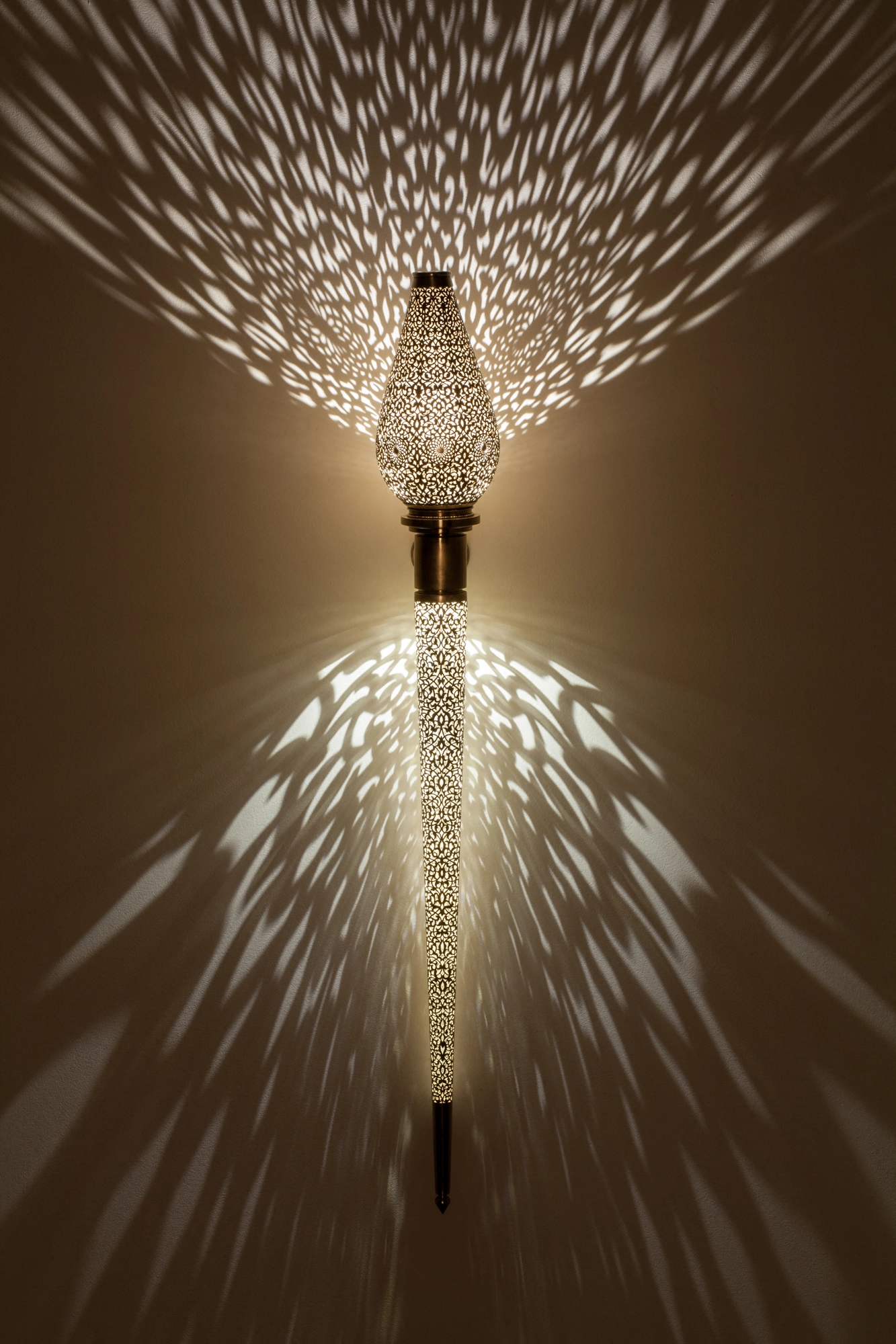 Tapering pierced-brass Treville torch wall light glowing, scattering a wide feathered burst of light up and down.