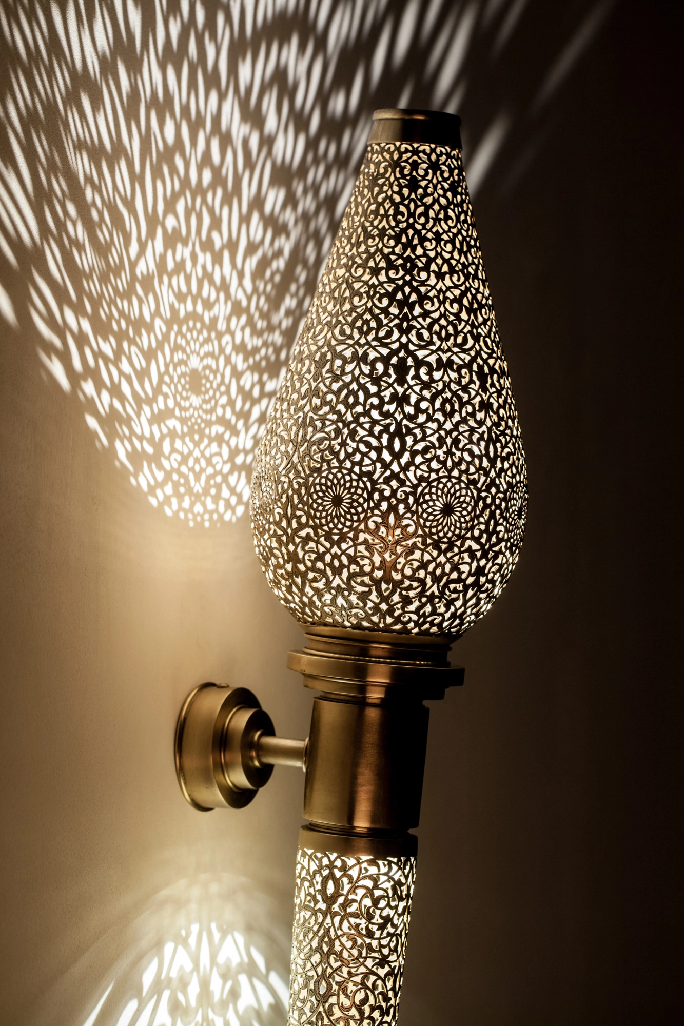 Close-up of a pierced-brass Treville torch head on its bracket, glowing and casting light across the wall.