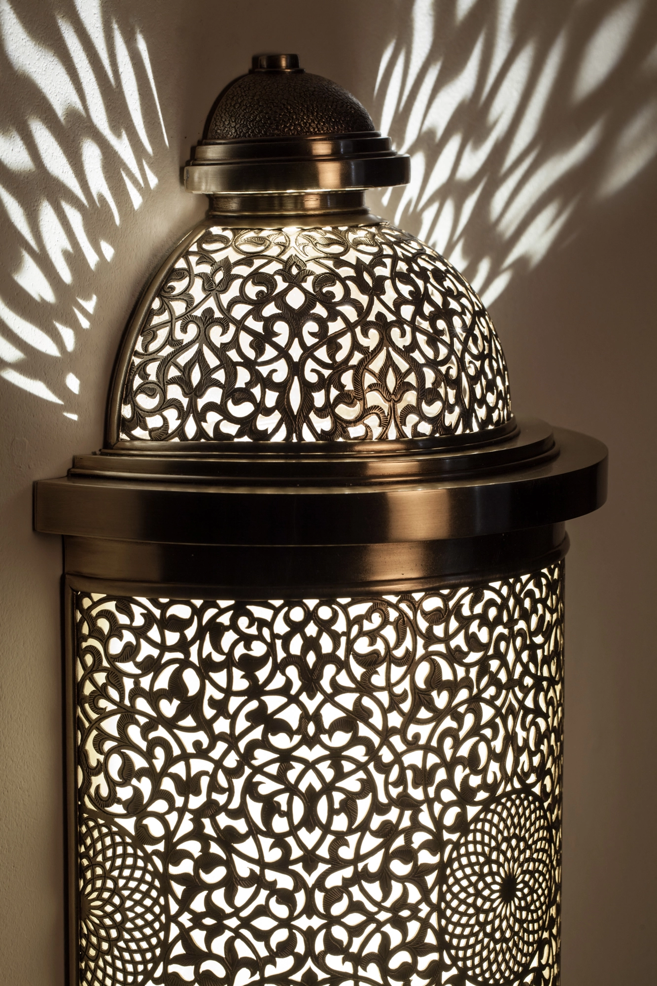 Close-up of a pierced-brass barrel lantern with a domed top, its dense fretwork glowing against shadow.