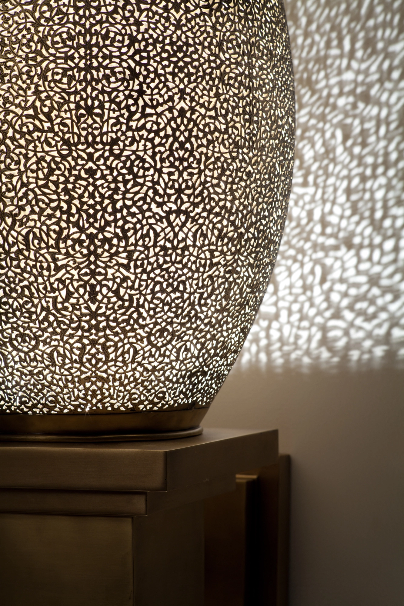 Close-up of a pierced-brass seated-flame wall light's bulb, its dense perforations glowing against scattered light.