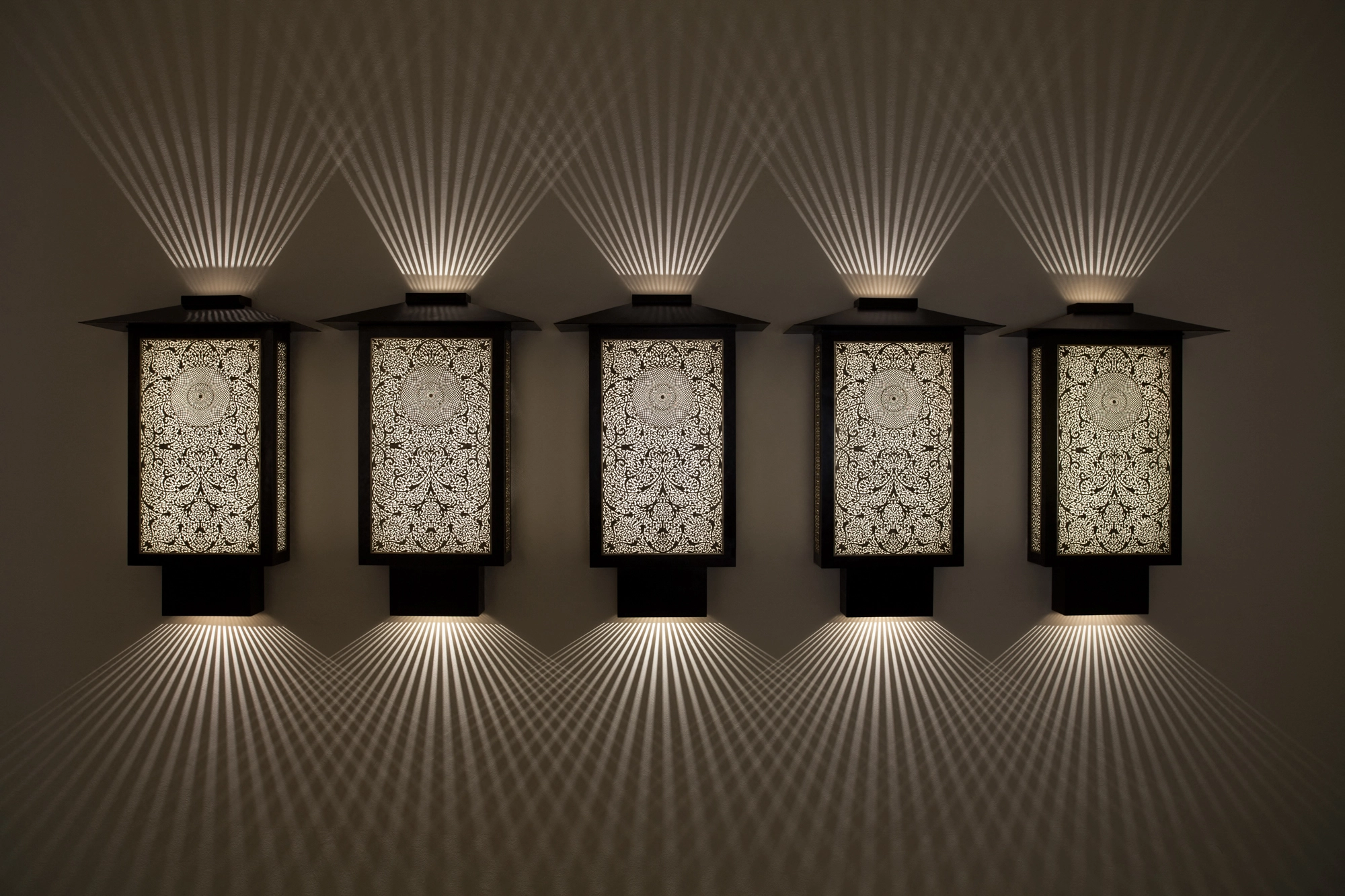 Five small pierced-brass oriental box wall lights in a row, glowing softly with downward light fans.