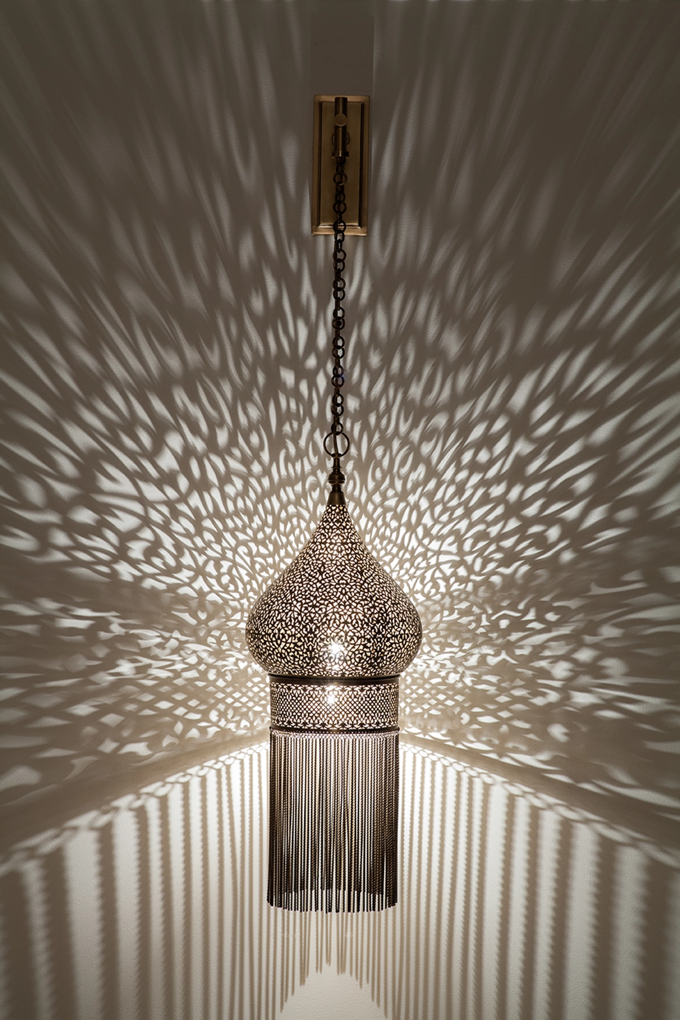 Pierced-brass dervish wall light with a long beaded skirt, glowing within a wide burst of light dots.