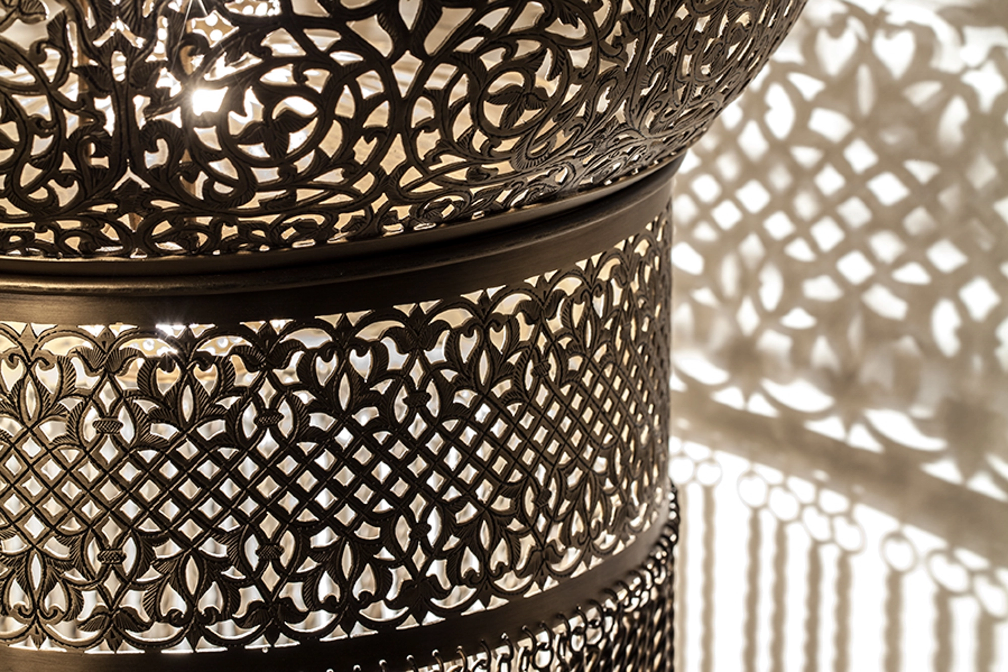 Close-up of a dervish wall light's pierced-brass dome, its dense fretwork catching warm light.