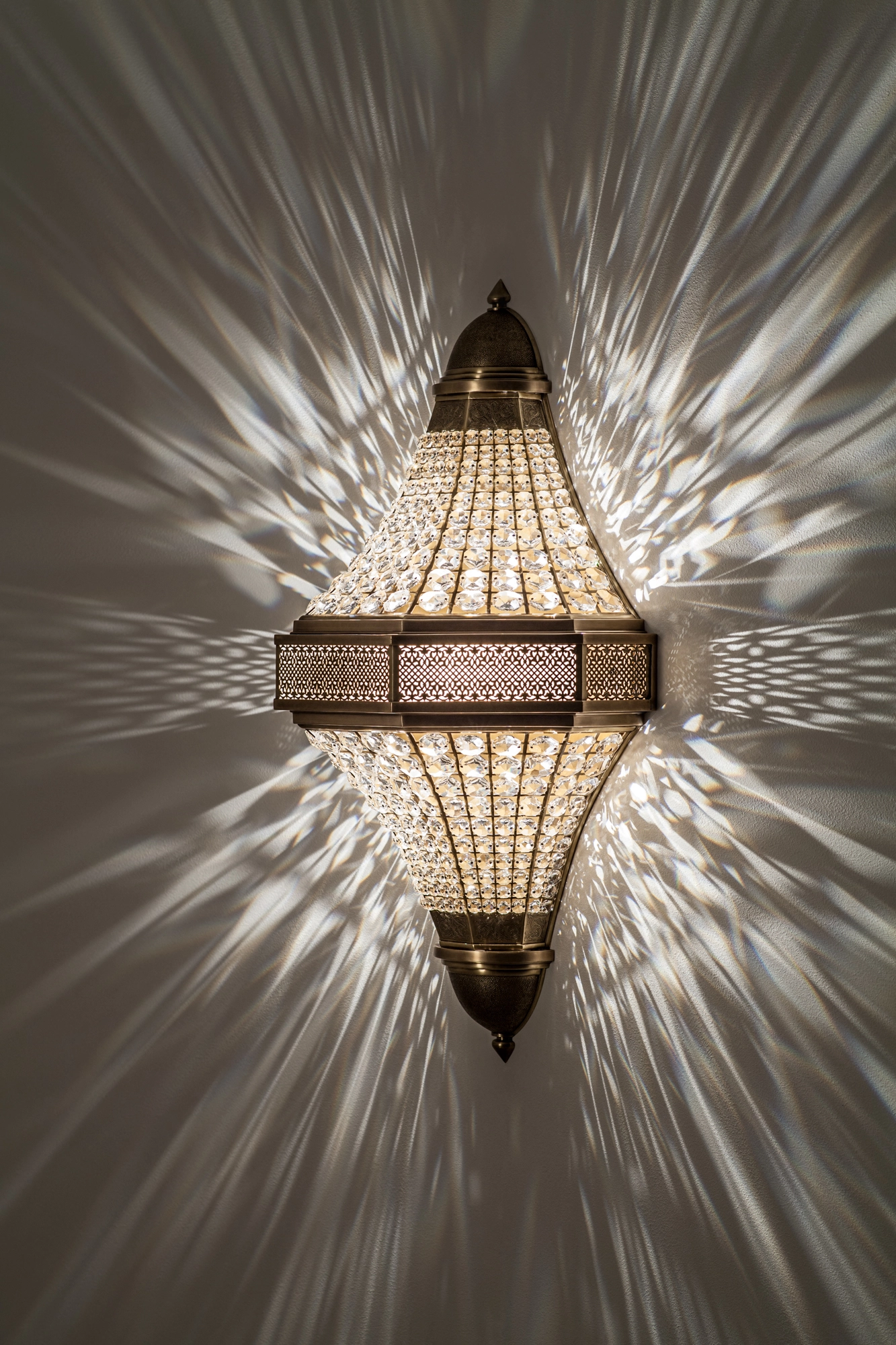 Diamond-shaped double-pyramid crystal wall light glowing brightly, radiating a starburst of light across the wall.
