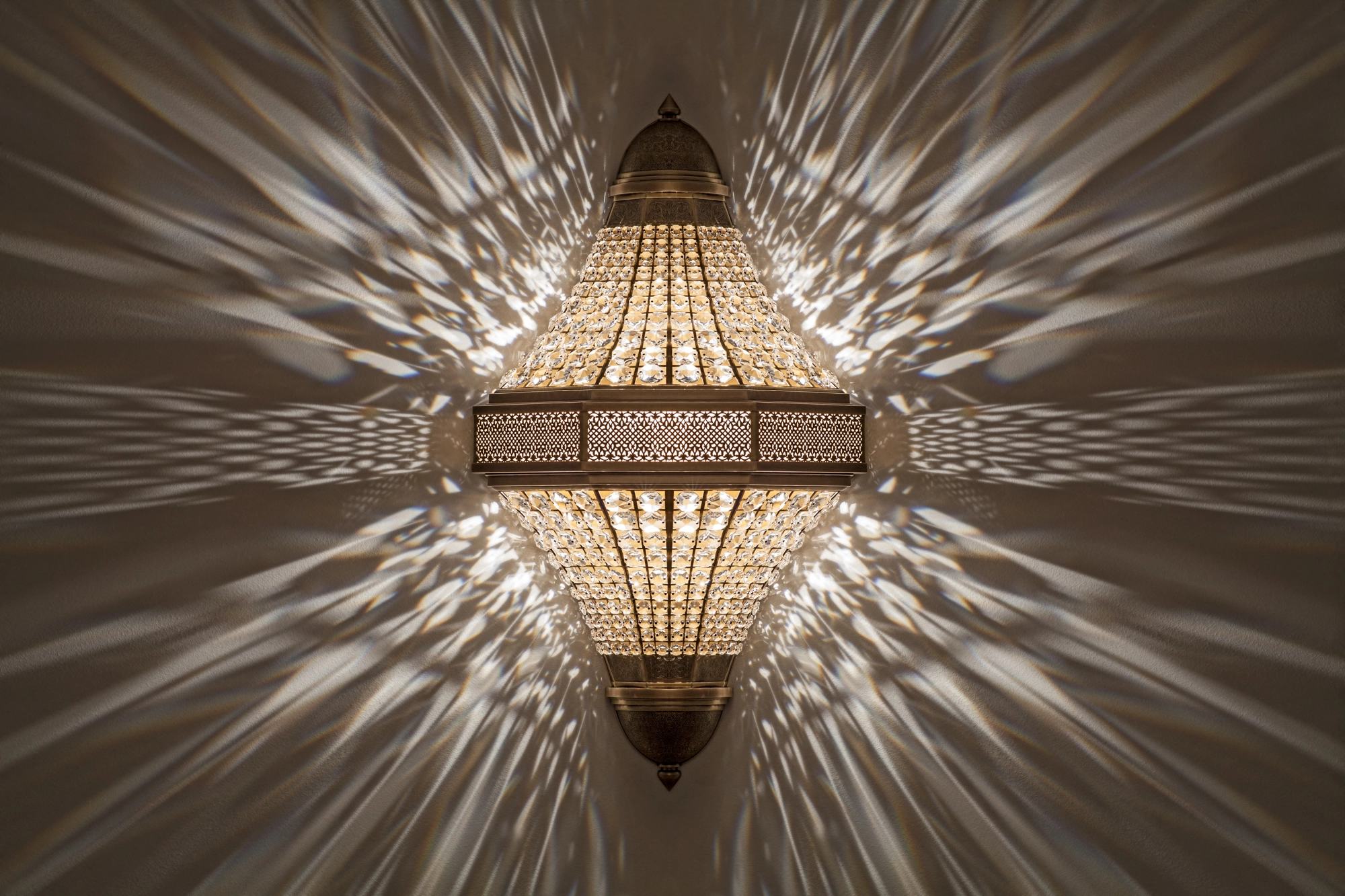 Double-pyramid crystal wall light glowing above its mirrored reflection, scattering rays of light outward.