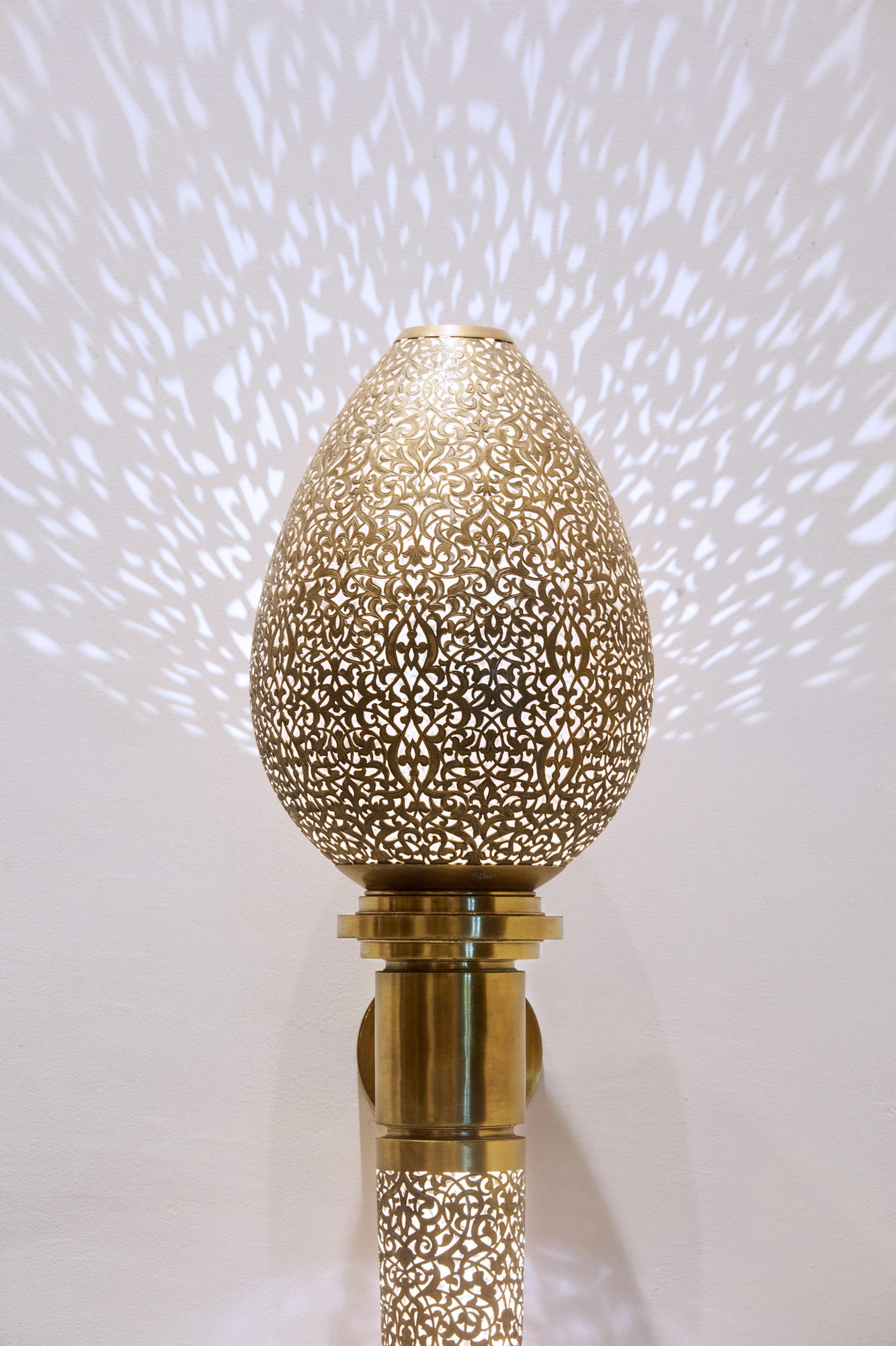 Illuminated egg-shaped pierced wall light scattering a starry pattern across the wall.