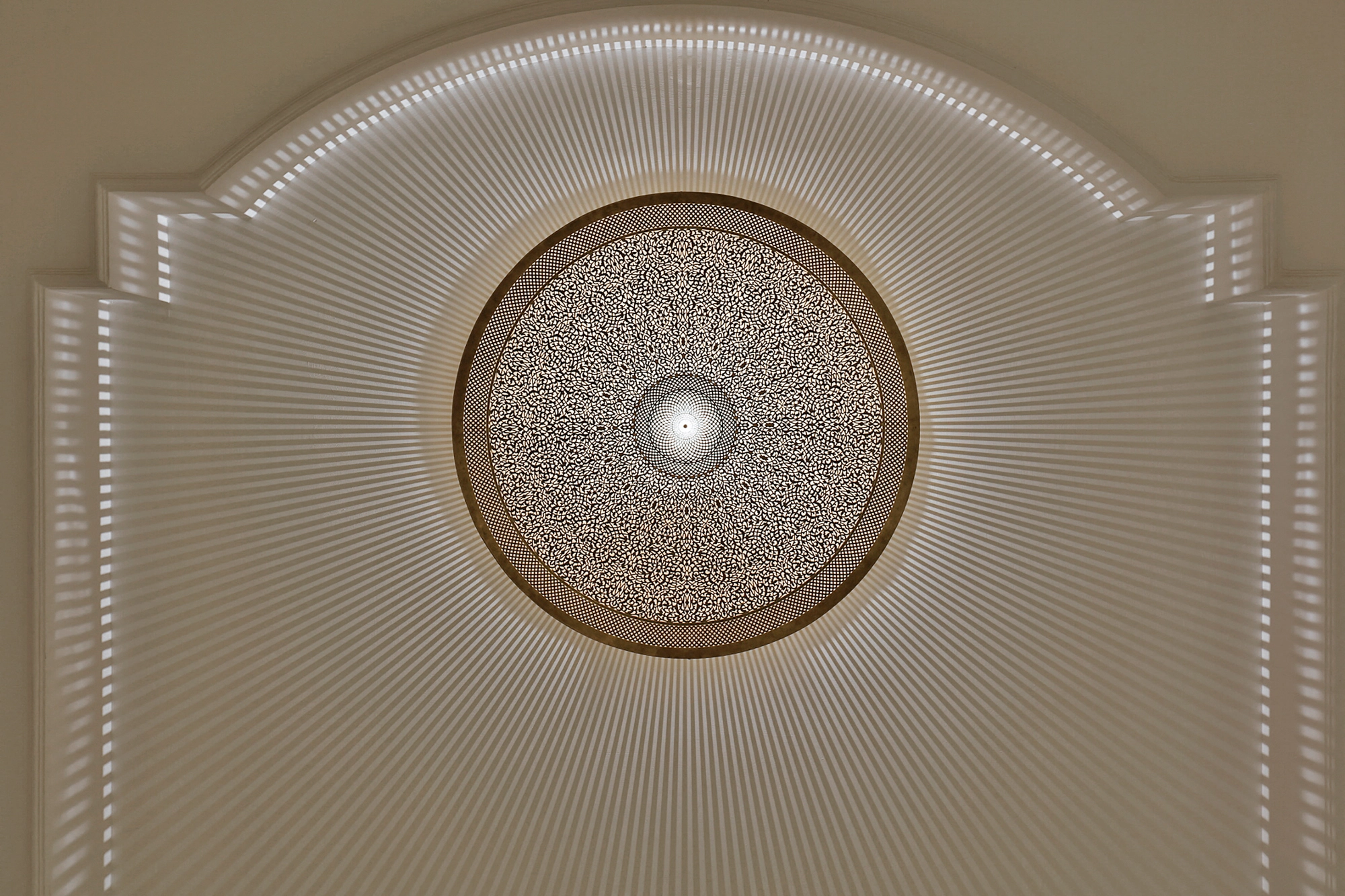 Glowing circular pierced-brass medallion set within an arched recessed panel, lit softly from within.