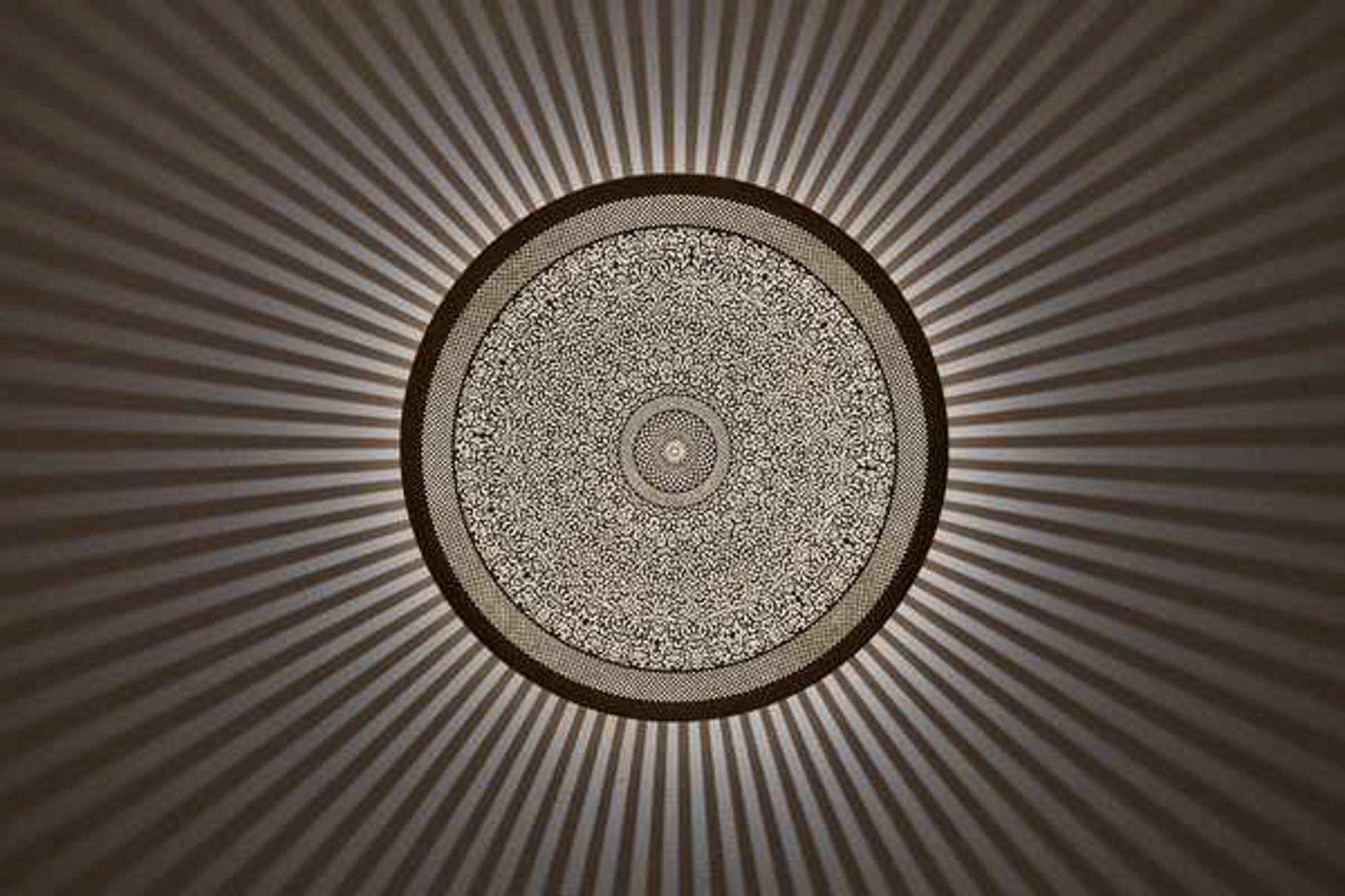 A round pierced metal medallion light casting a fine radial spray of light across a warm brown surface.