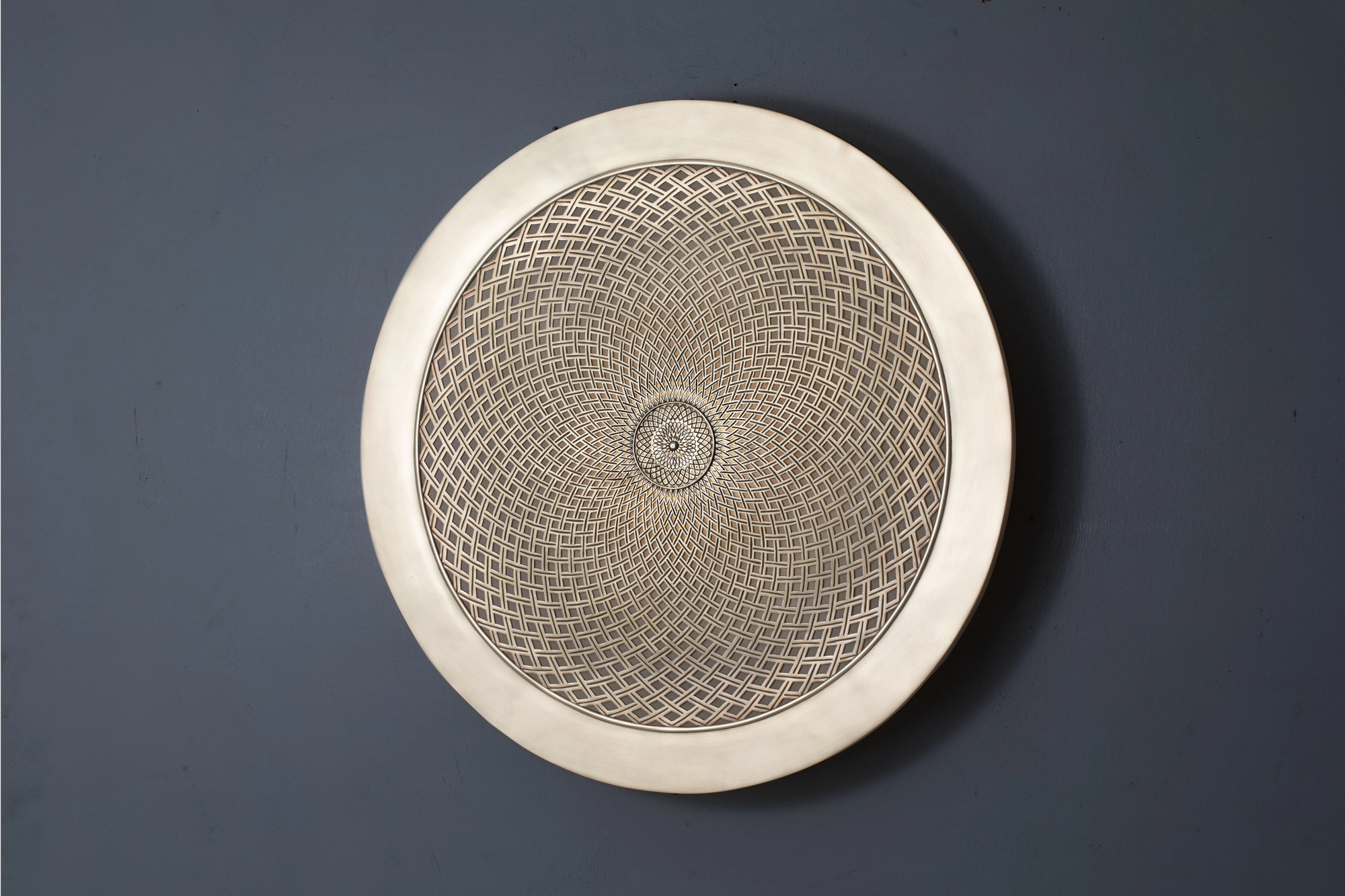 Round pierced-brass Fibonacci medallion wall light mounted flat on a blue-grey wall.
