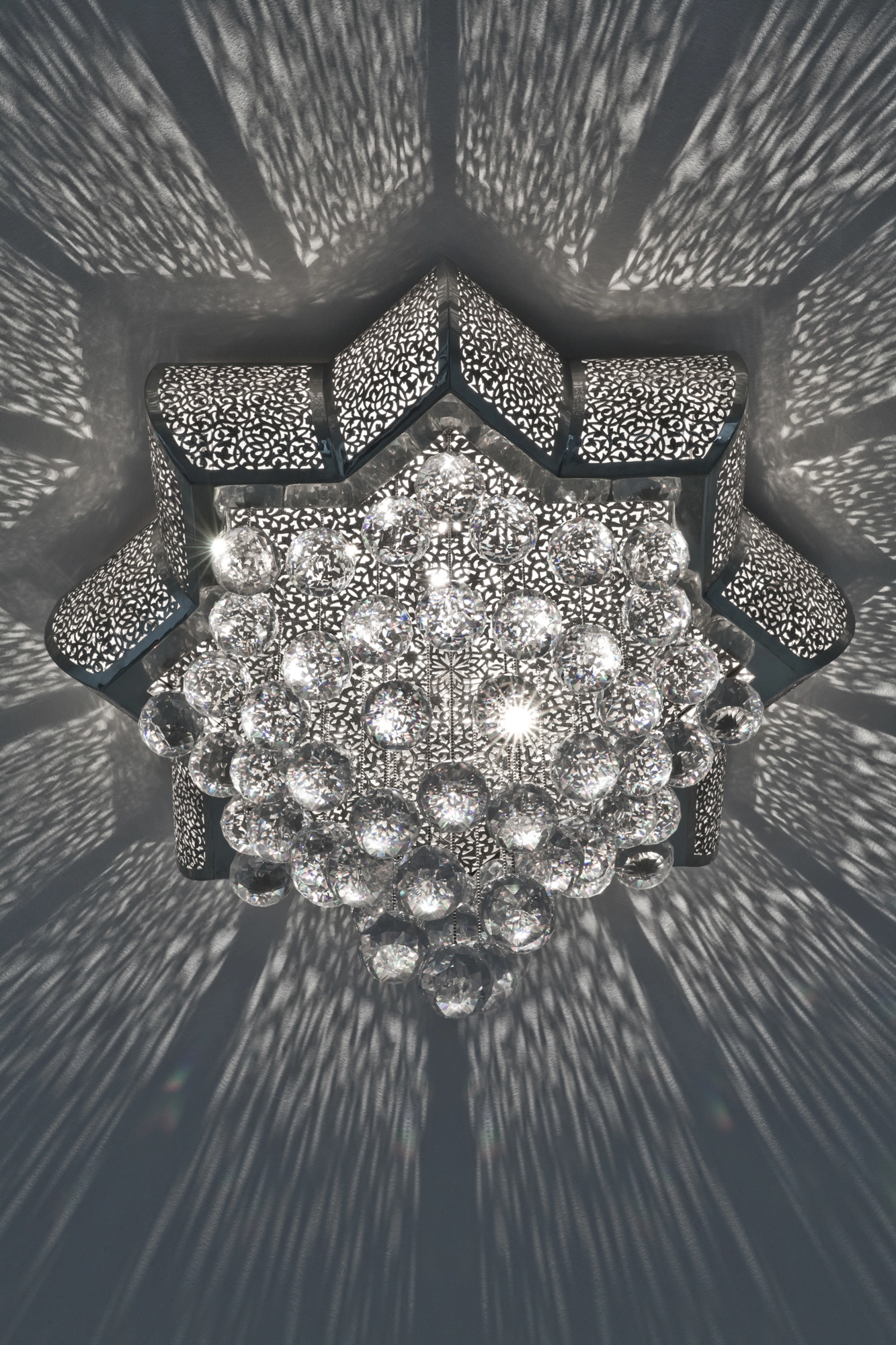 A large crystal cascade ceiling light with tiered hanging crystals beneath a pierced metal frame, seen from below.