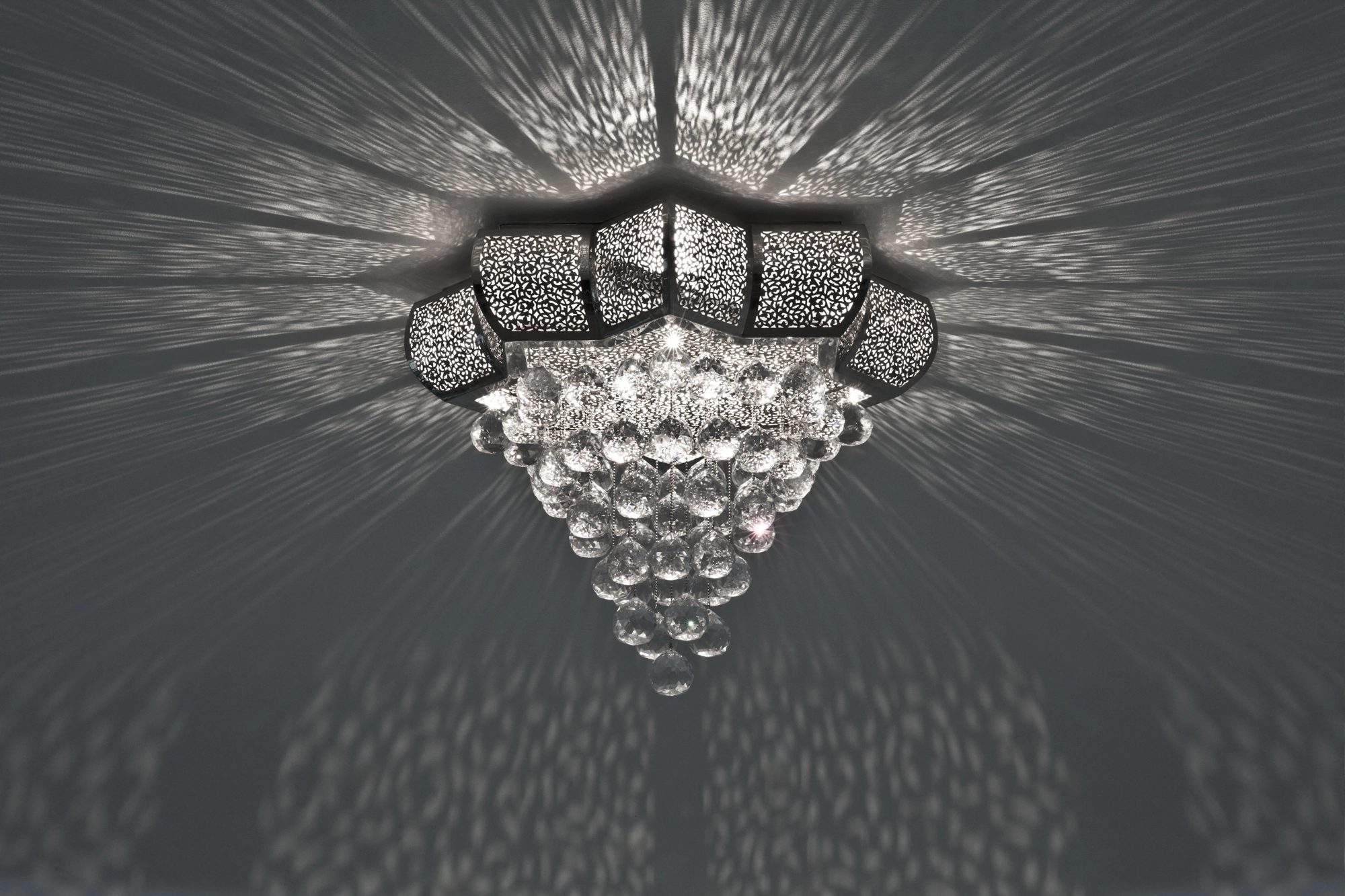 A crystal cascade ceiling light with a pierced metal ring and hanging crystals, seen from below on a grey ceiling.