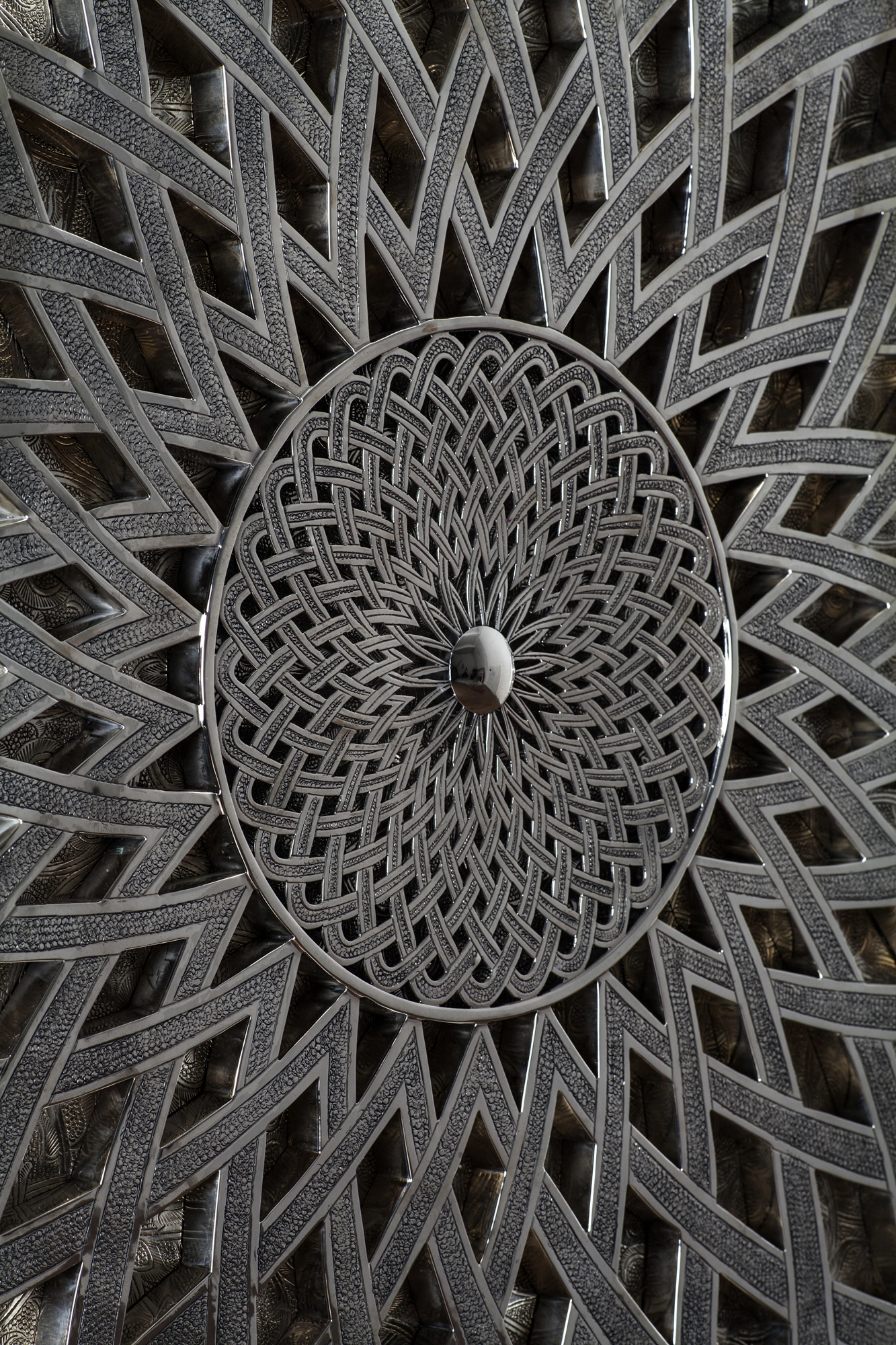 Close-up of a silver wall panel's radiating star pattern of interwoven metal bands around a woven centre.