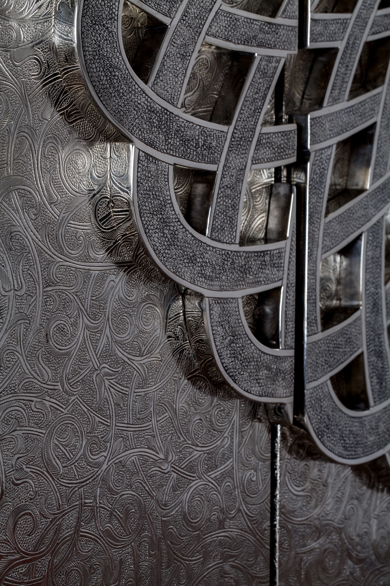 Close-up of curved interwoven metal bands and an engraved ground on a silver wall panel.