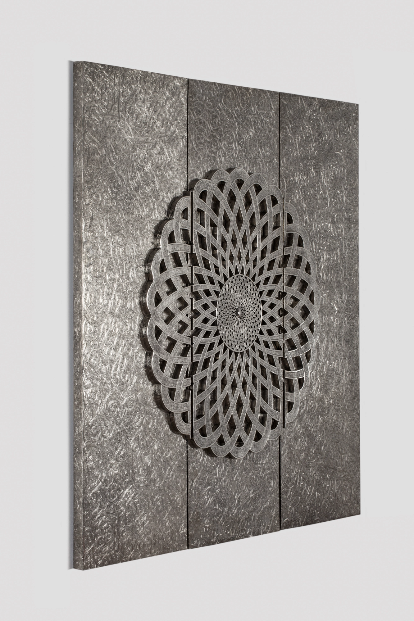 A silver textured three-panel wall artwork centred on a circular geometric rosette motif, on a grey background.