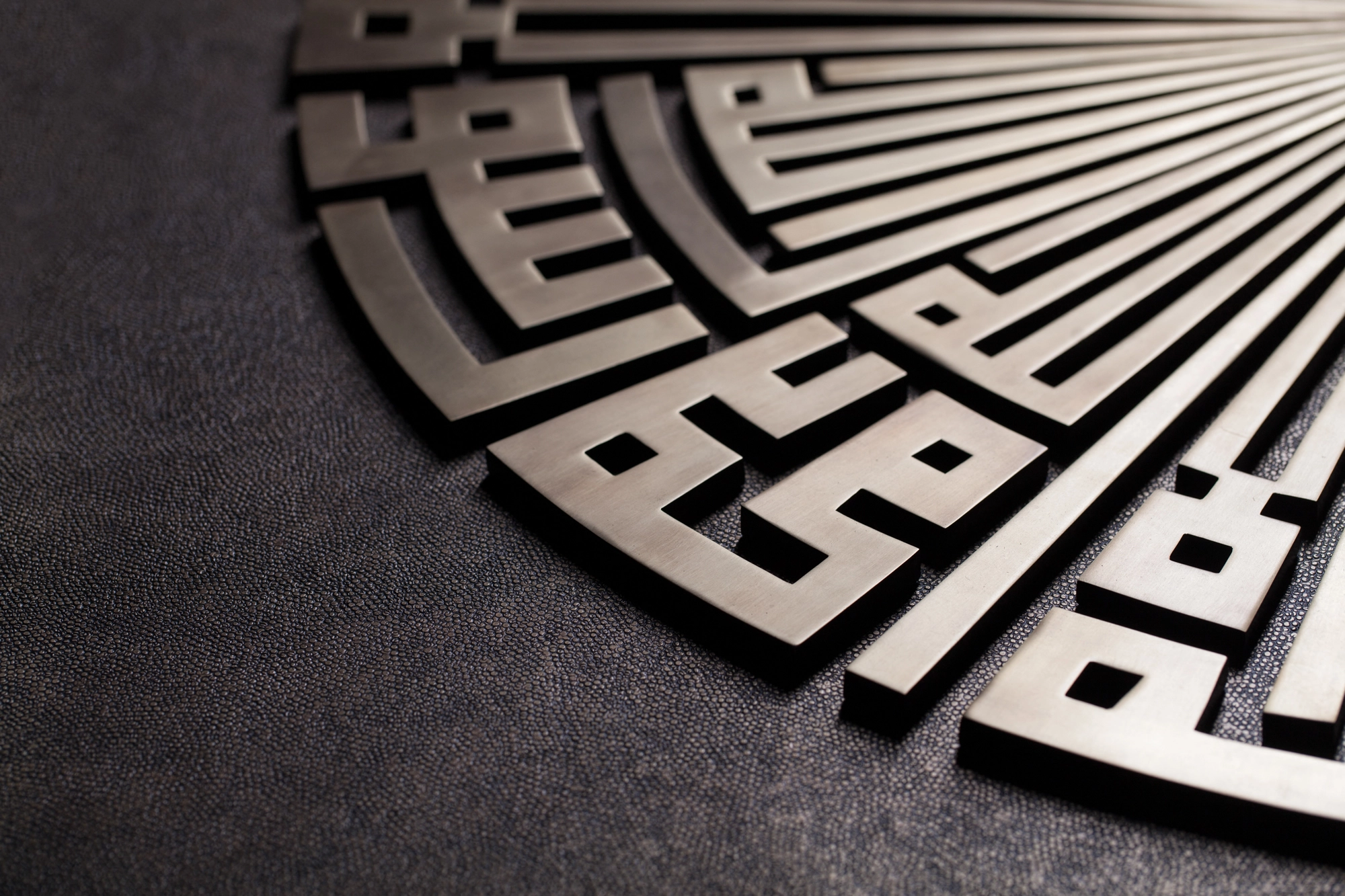 A quarter-circle fan of angular Kufic metalwork seen at an angle against a dark ground.