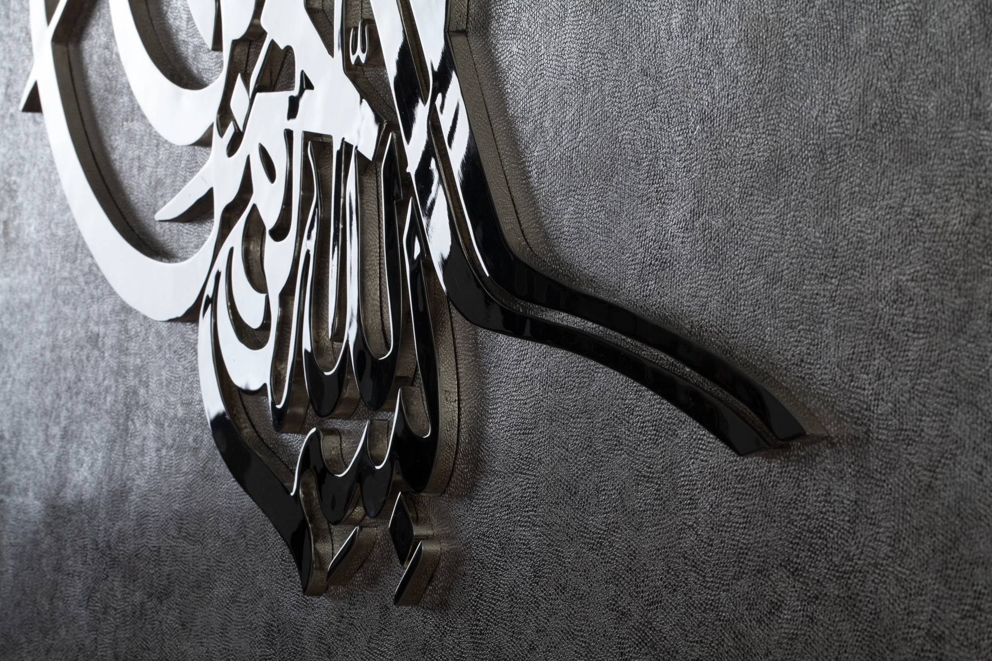 Angled close-up of interwoven metal calligraphic strokes on a textured grey wall panel.