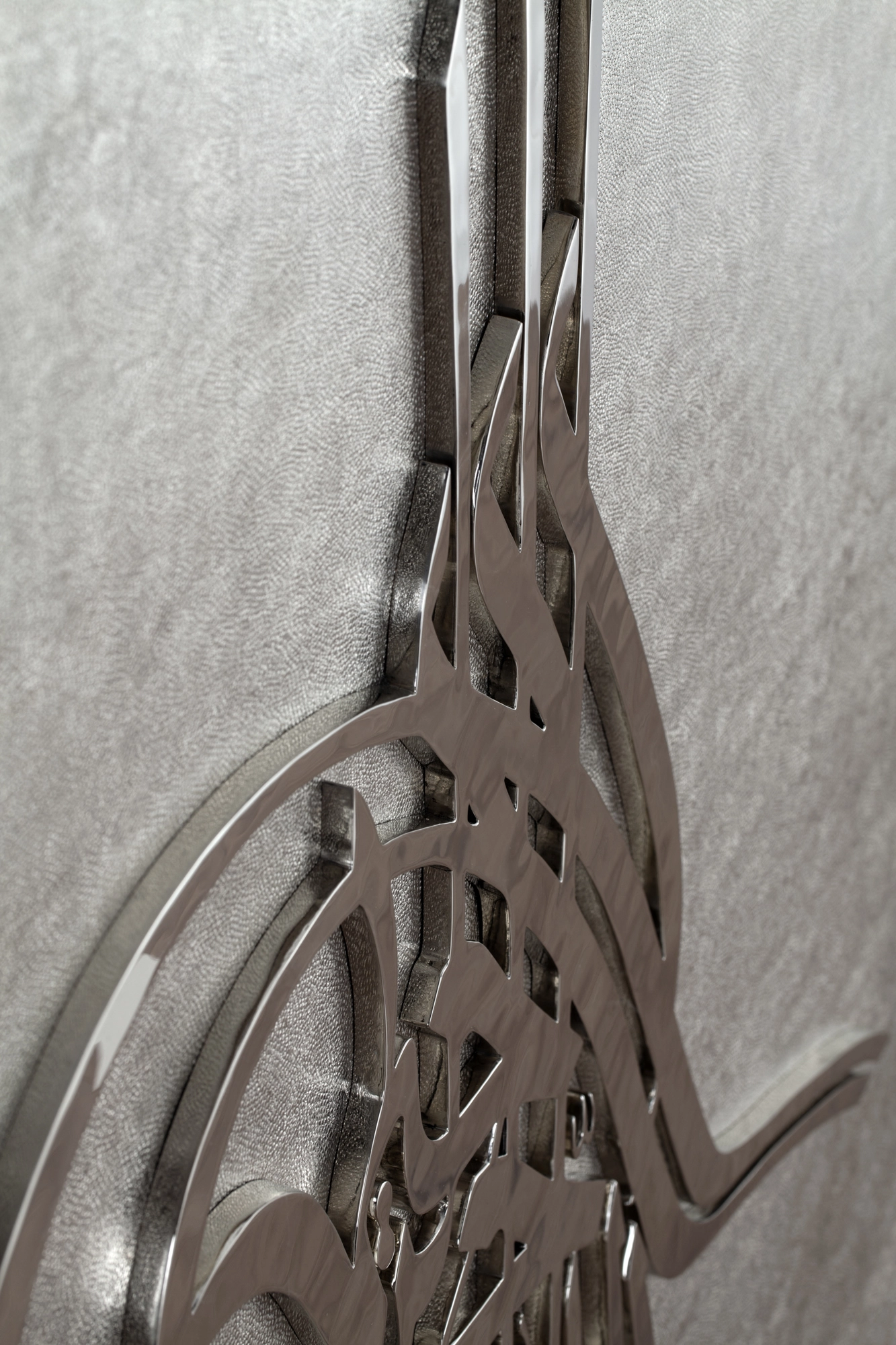 Close-up of intertwined metal calligraphy with a looping curve on a pale textured panel.