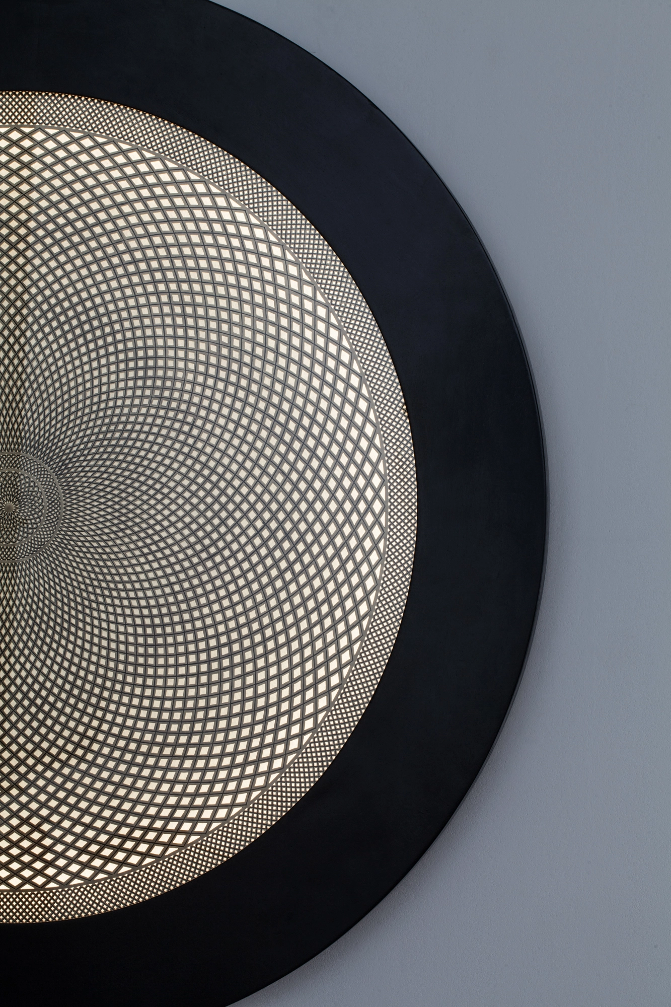 Close-up of a backlit wall disc showing the finely perforated golden surface meeting its black ring frame.