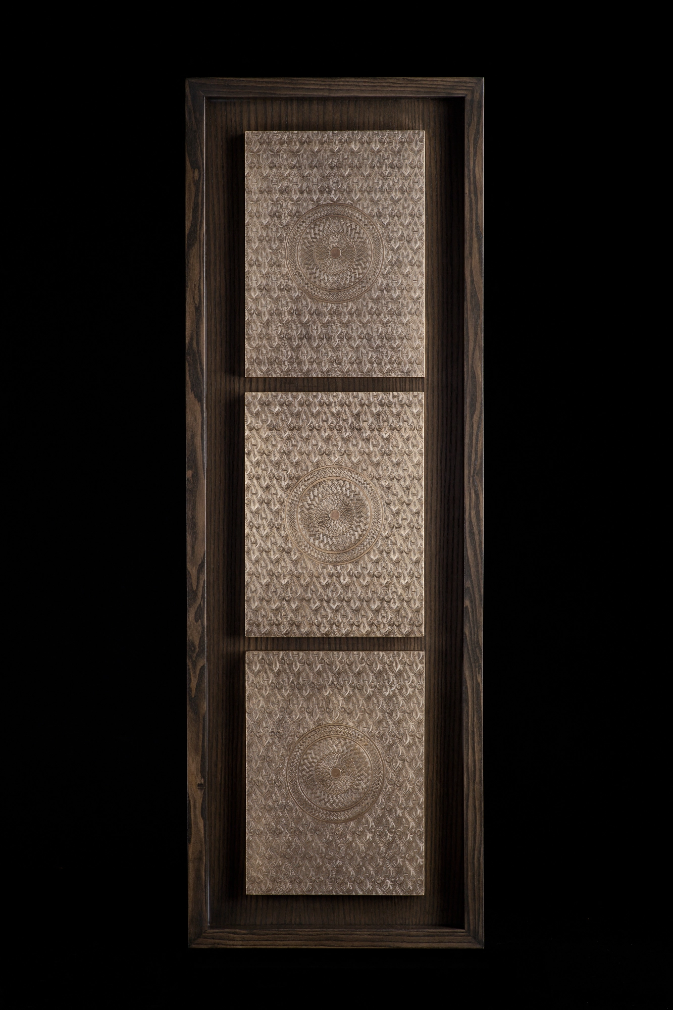 A tall dark frame holding three stacked pale engraved medallion panels, against a black background.