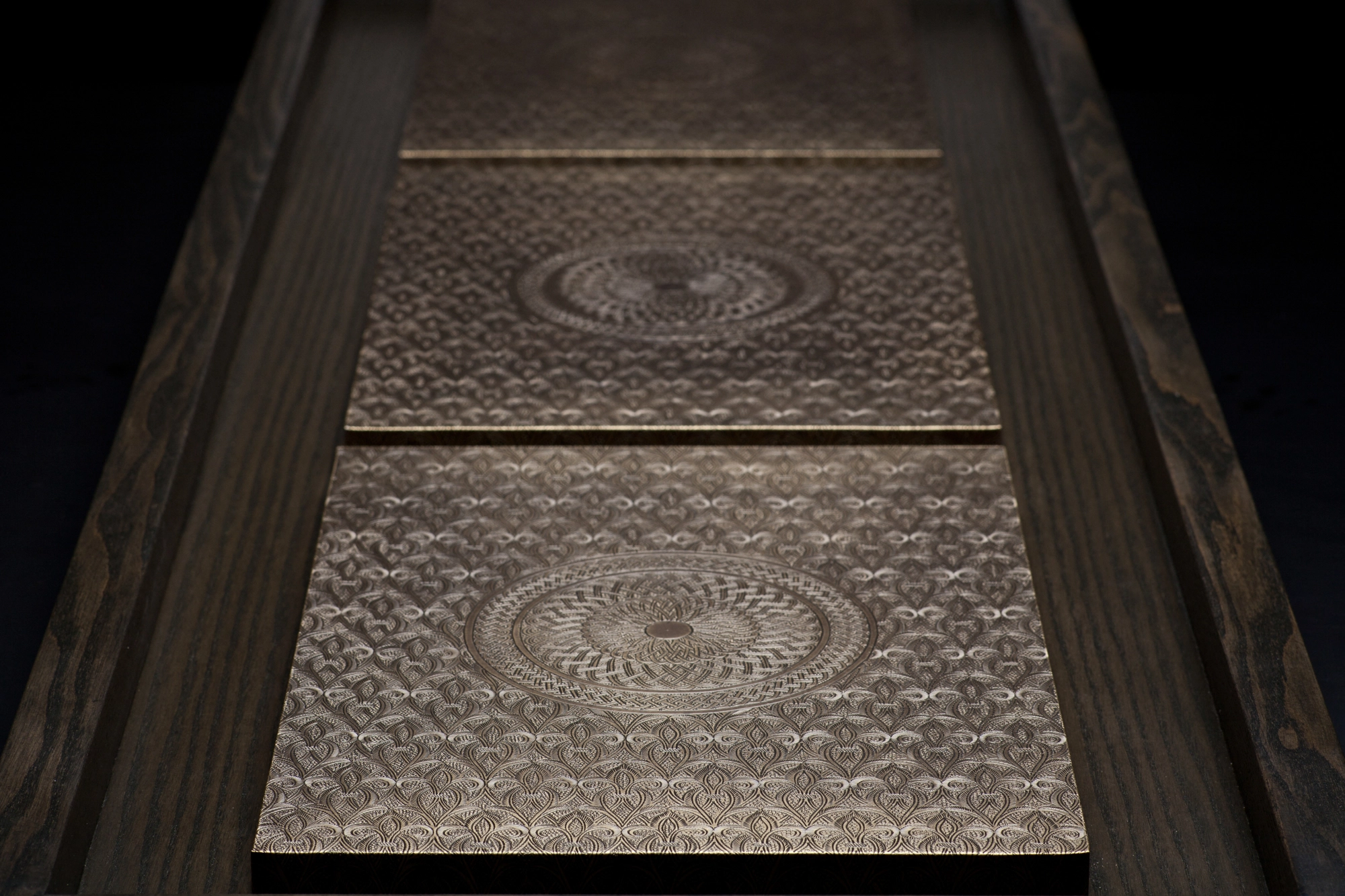 An angled view of framed pale engraved panels separated by dark dividers, dimly lit.