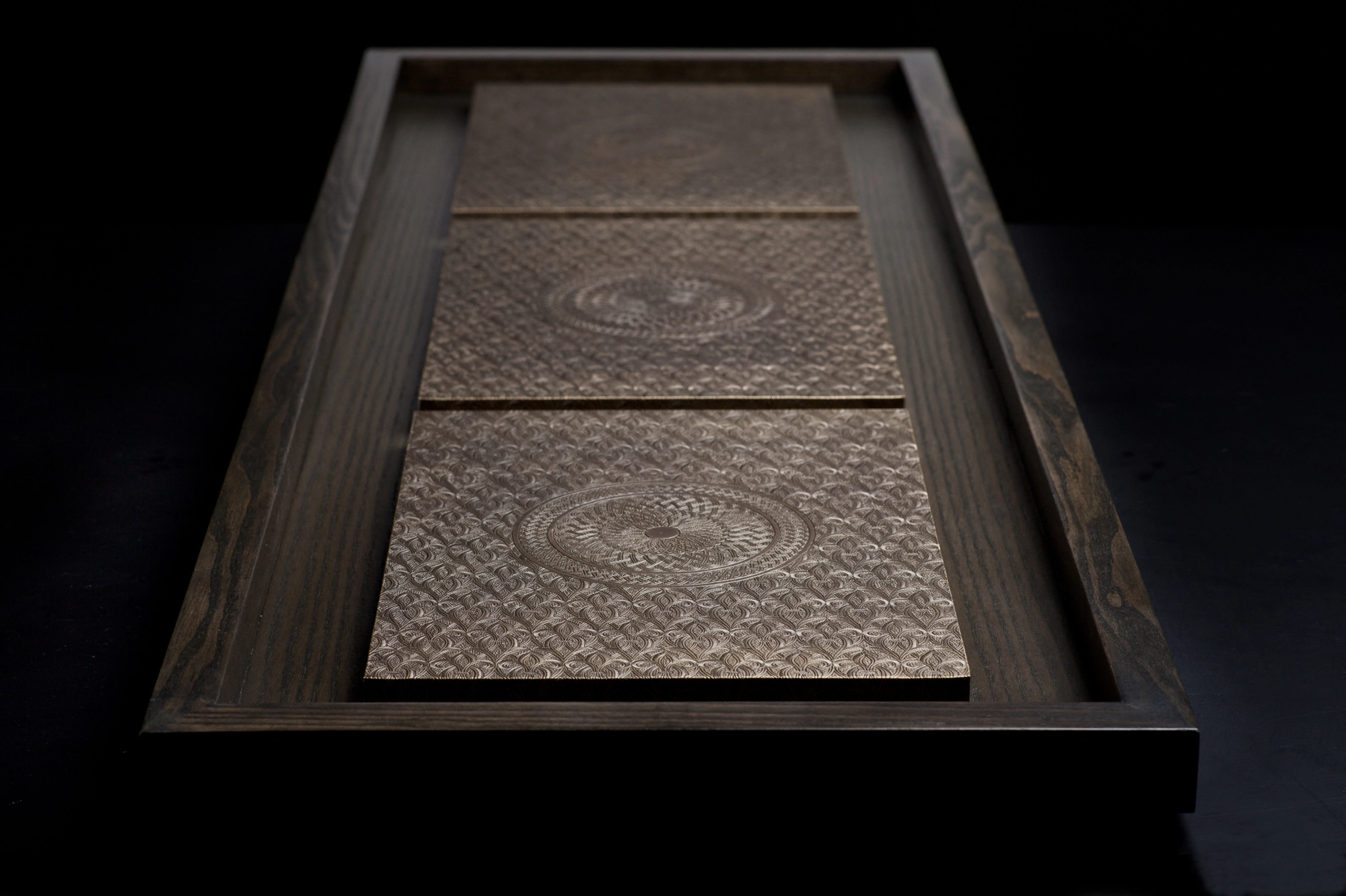 A low-angled view of a dark frame holding three pale engraved medallion panels.