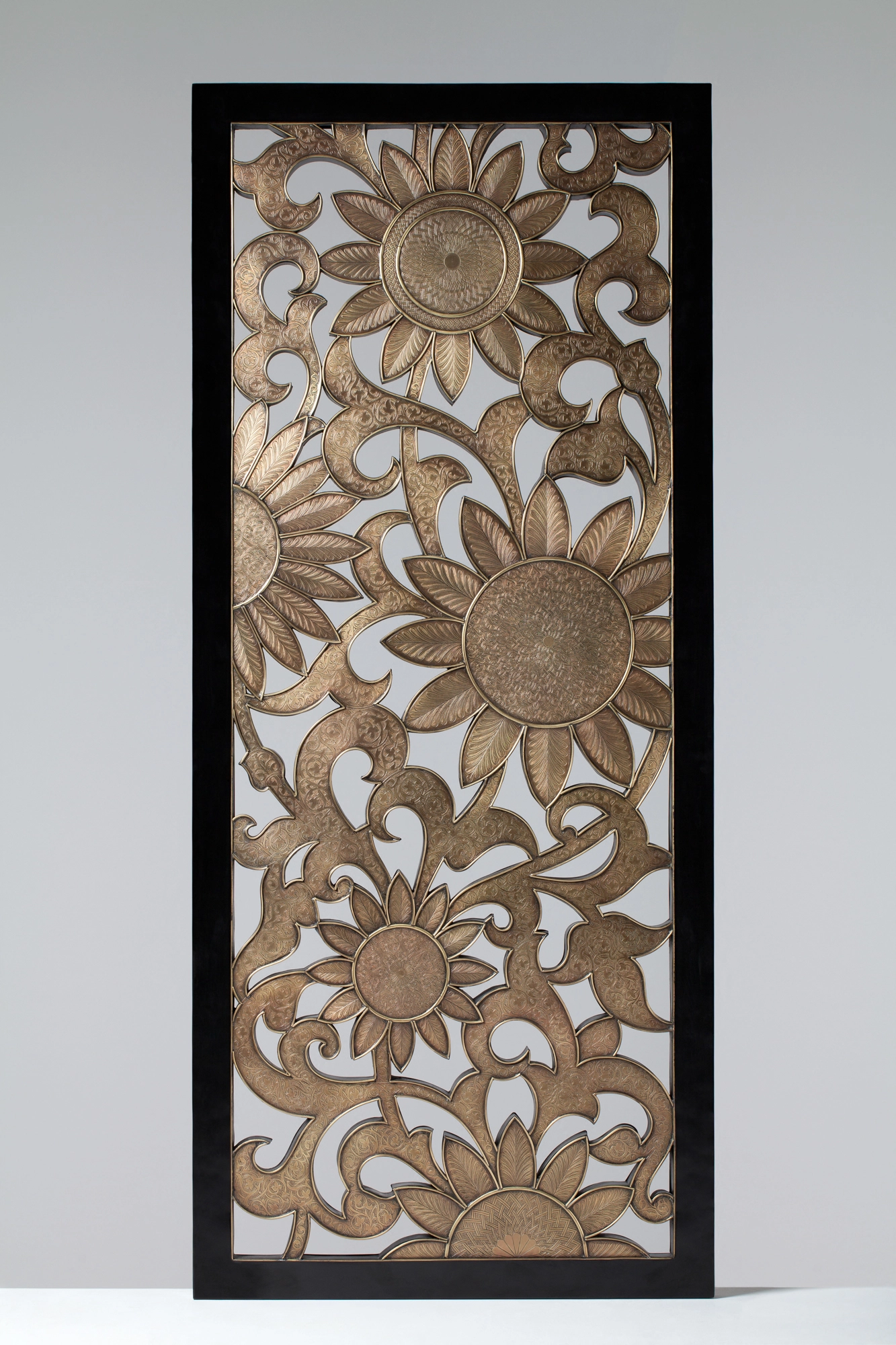 A tall carved wooden panel of openwork sunflowers and foliage set in a black frame.