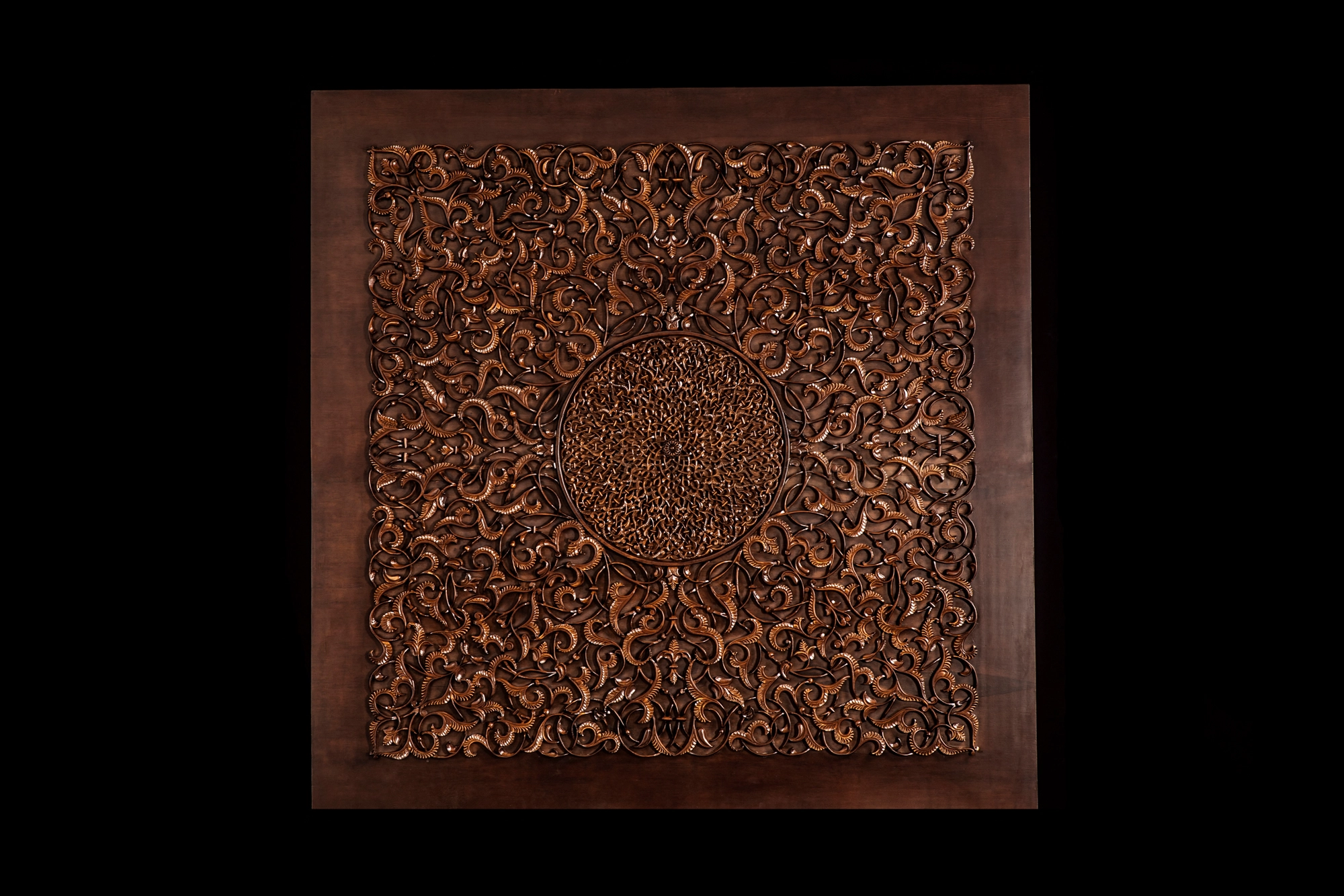 A framed square panel of carved dark-wood floral openwork, lit against a black background.