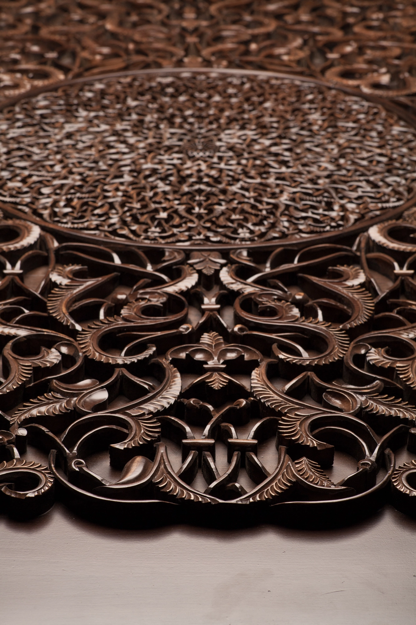 An angled view of a carved dark-wood panel with a circular medallion, lit from below.