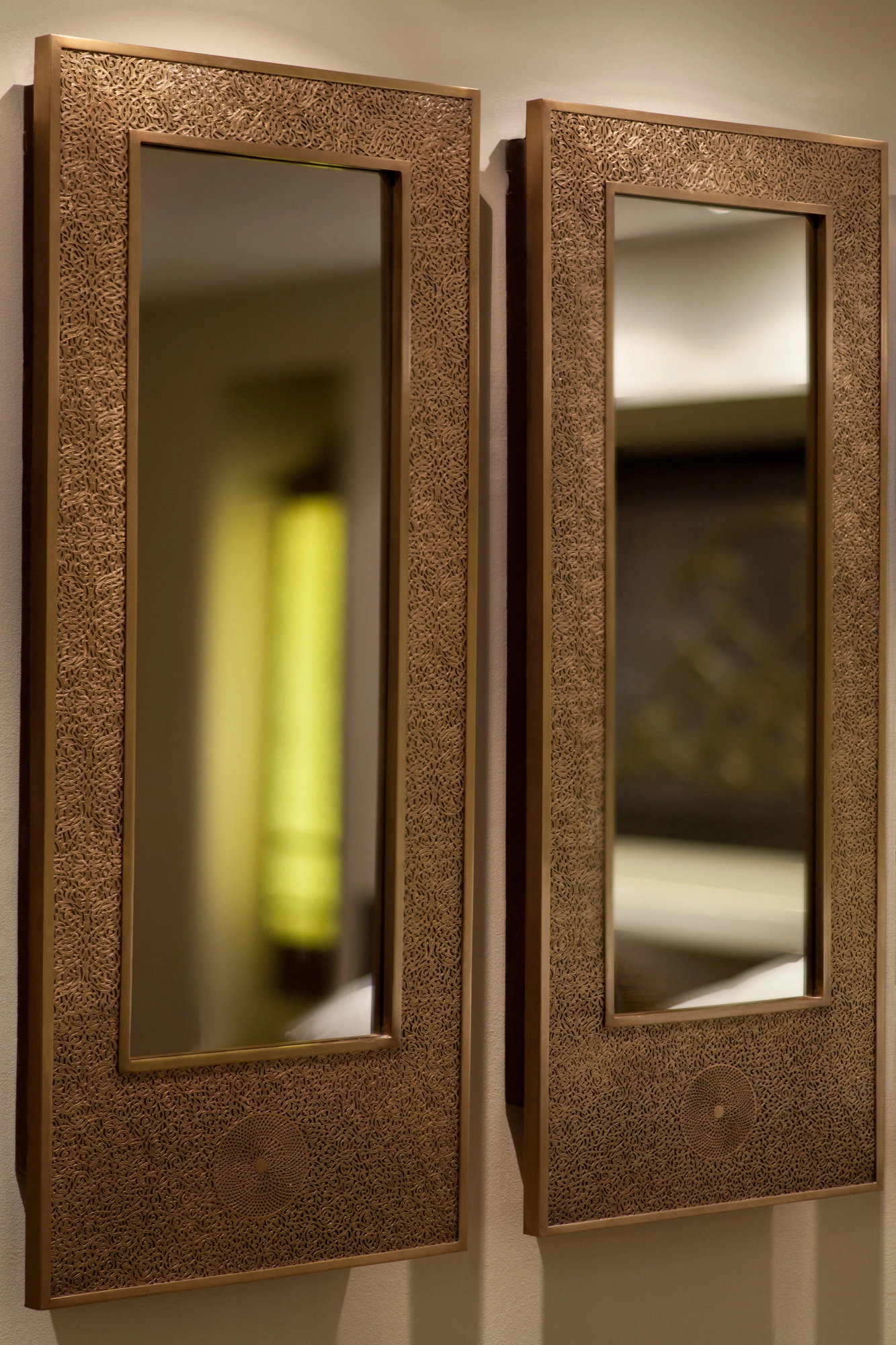 Two tall rectangular mirrors in engraved golden frames, reflecting a glowing green vase nearby.