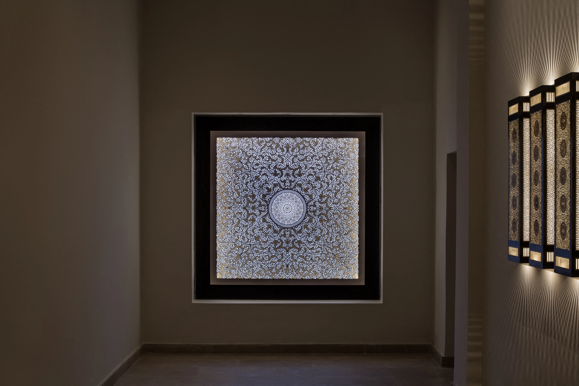 A framed square backlit panel glowing on the wall of a dim, warmly lit hallway.