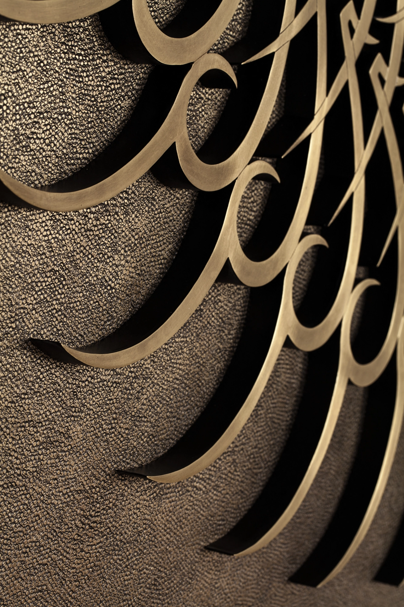 Close-up of golden calligraphic swirls raised over a finely textured dark ground.