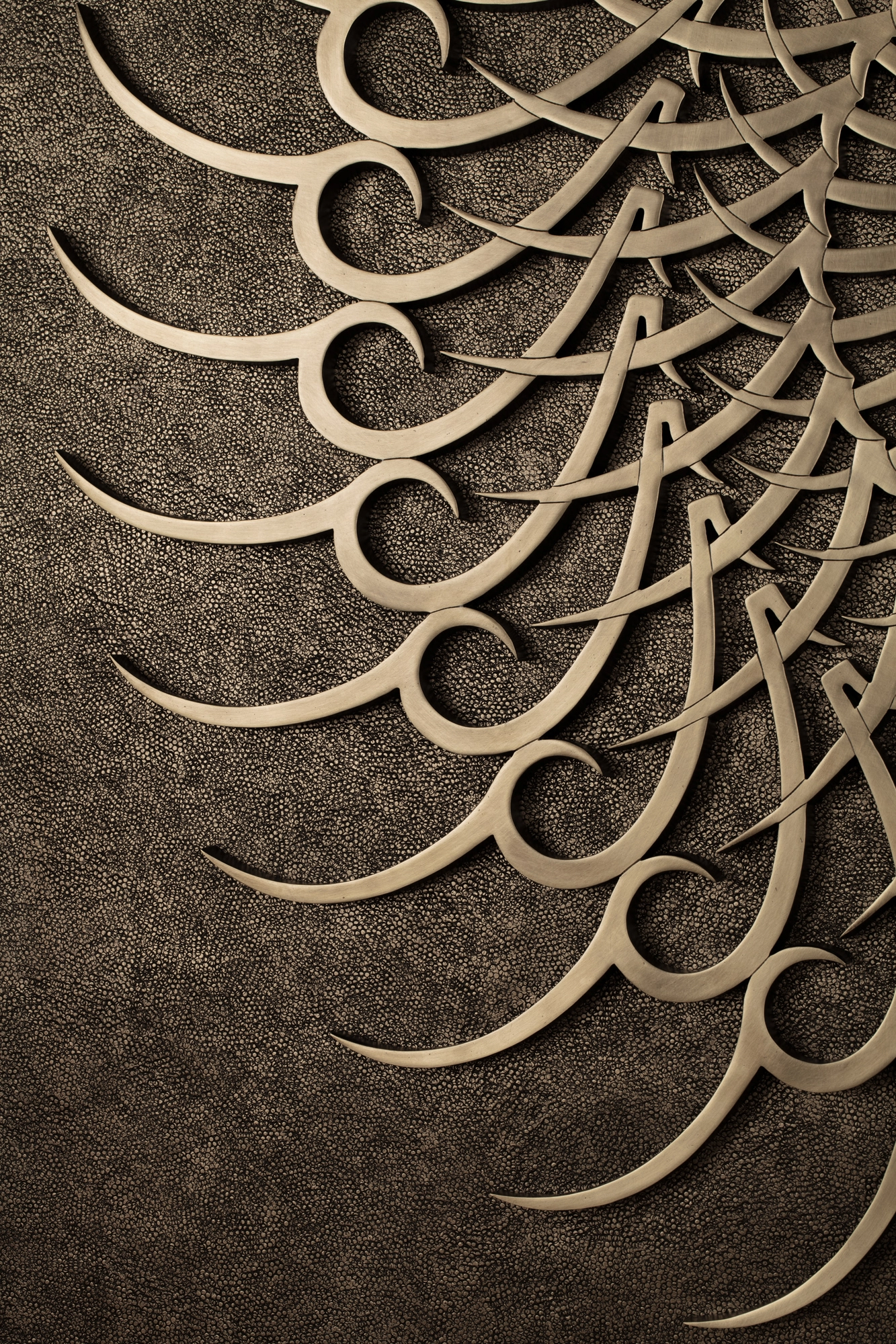 Close-up of radiating golden calligraphic swirls forming a spiral on a textured panel.
