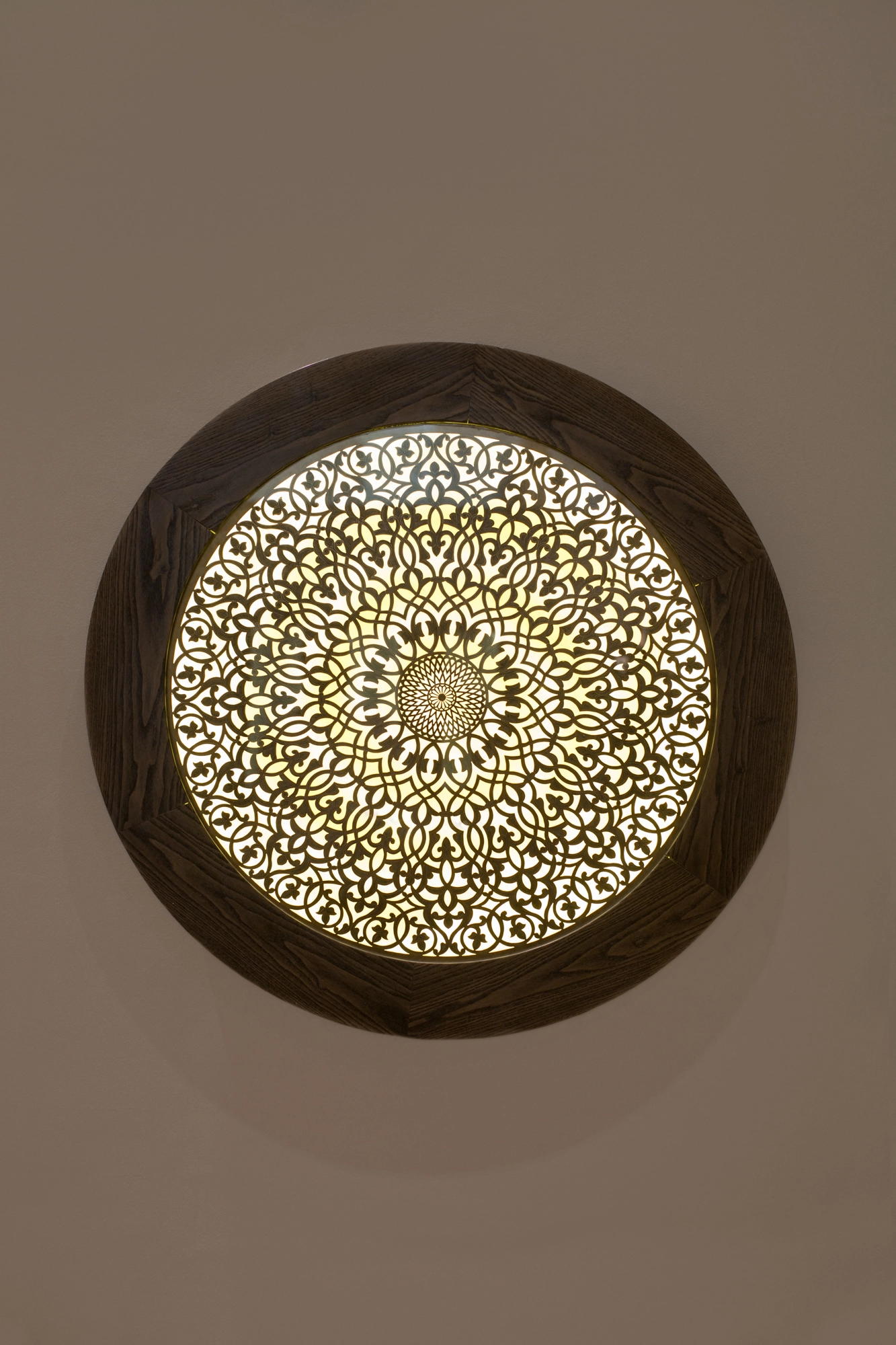 A round backlit wall panel with an intricate gold and green star pattern set in a dark circular wood frame.