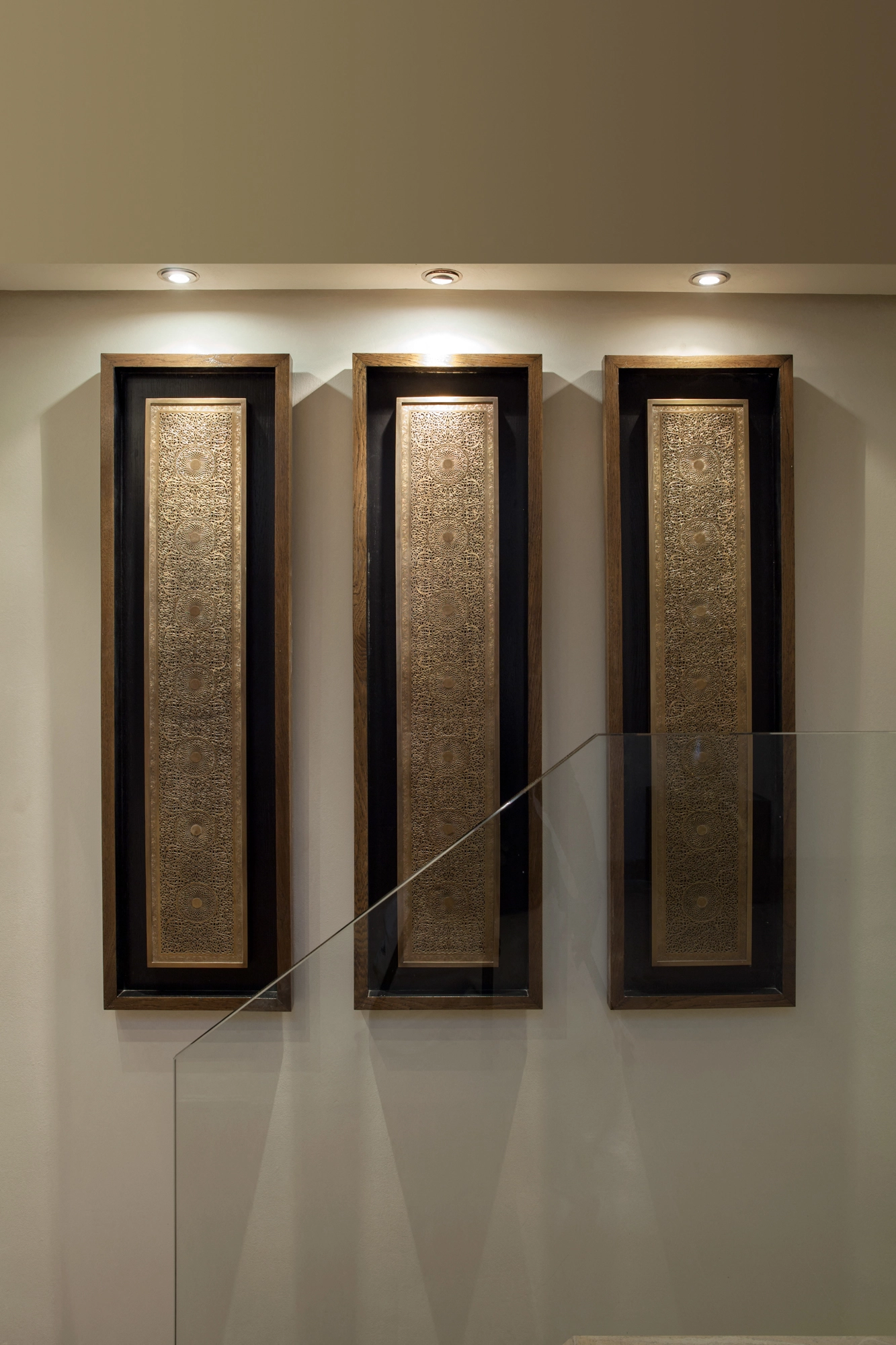 Three tall vertical framed calligraphy panels mounted side by side on a wall, lit from above.