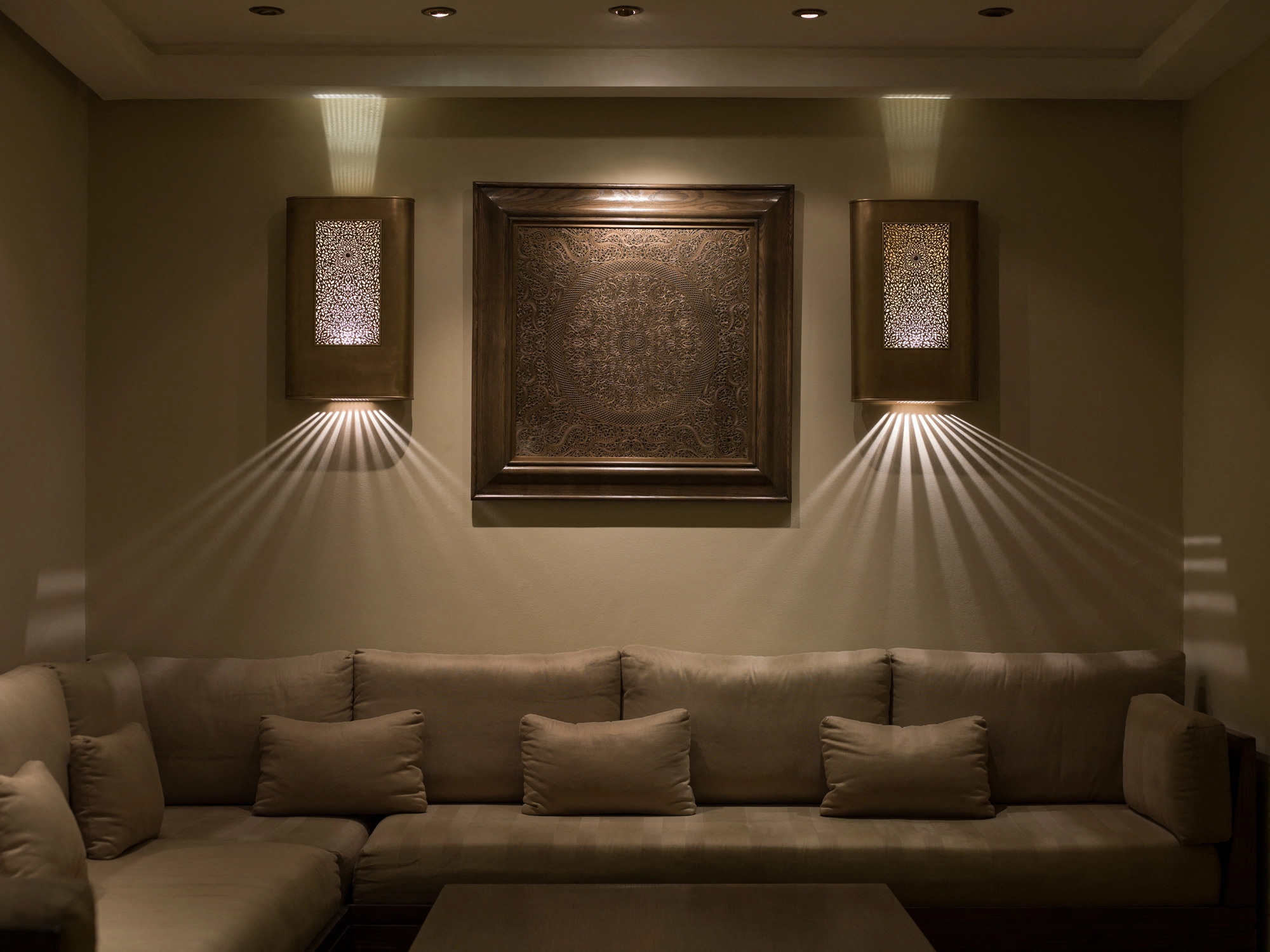 A sitting room with a framed artwork flanked by two backlit panels above a long sofa, softly downlit.