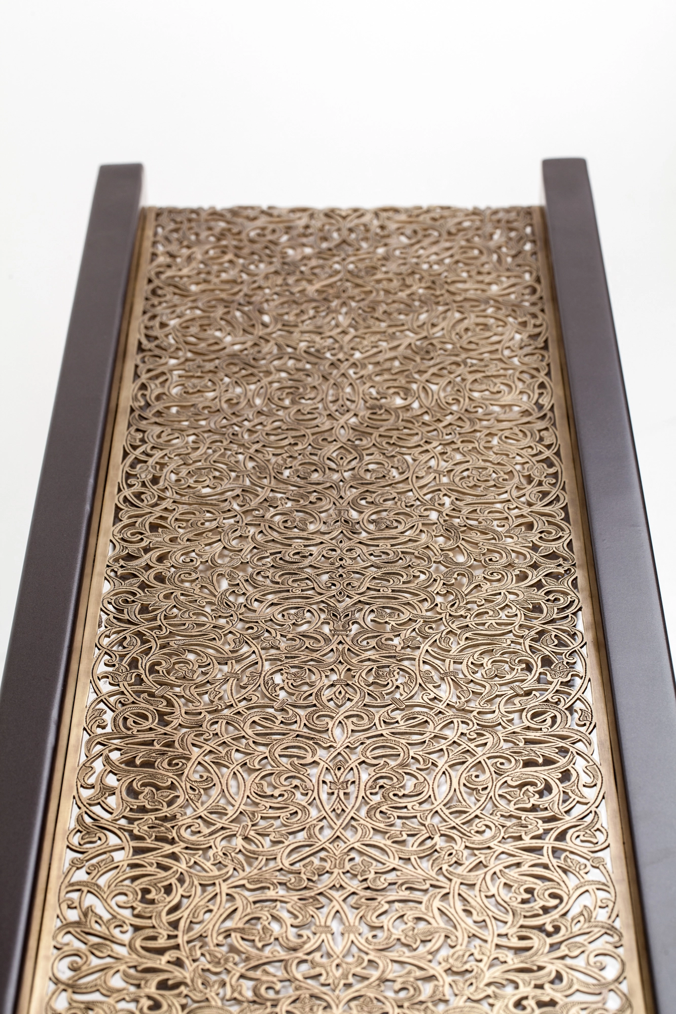 A view along the top of a console table showing its pierced golden patterned runner between dark edges.