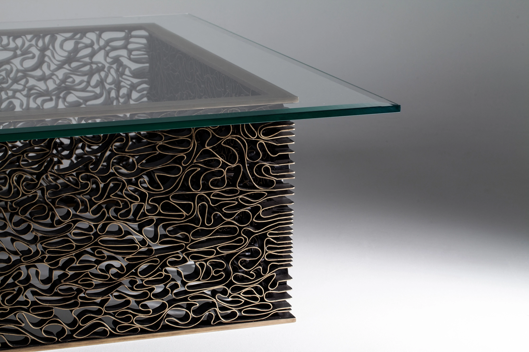 A glass-topped coffee table on a base of tangled wavy metal strands, seen at an angle on a grey background.