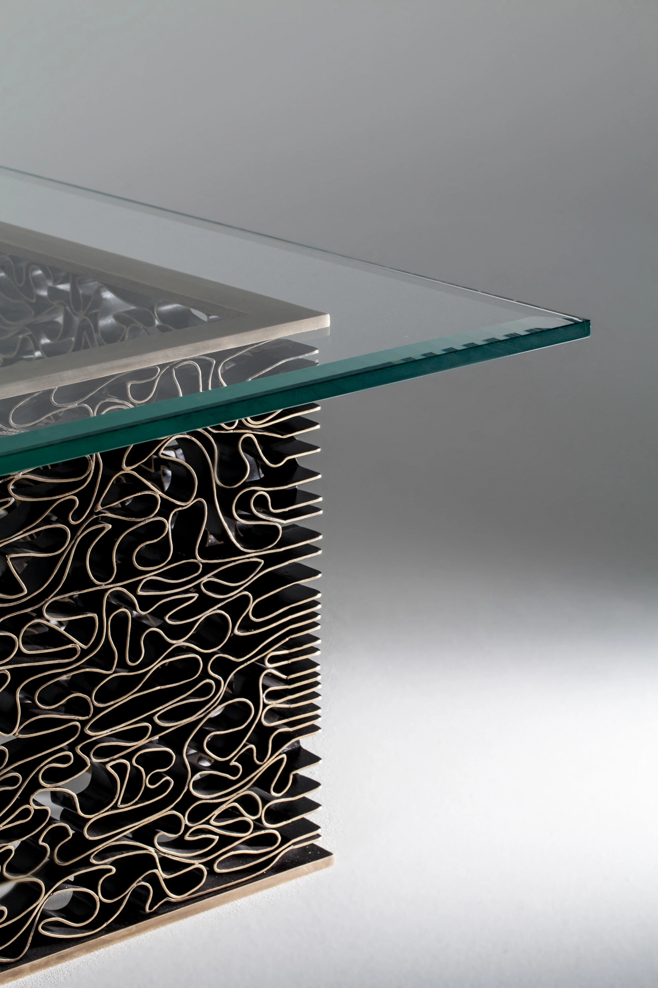 A glass-topped coffee table on a dense tangle of wavy metal strands, seen at a low angle on grey.