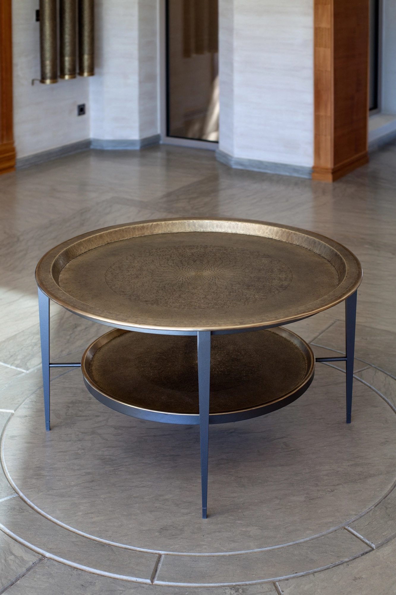 Round two-tier brass occasional table set on a circular stone floor medallion among archways.