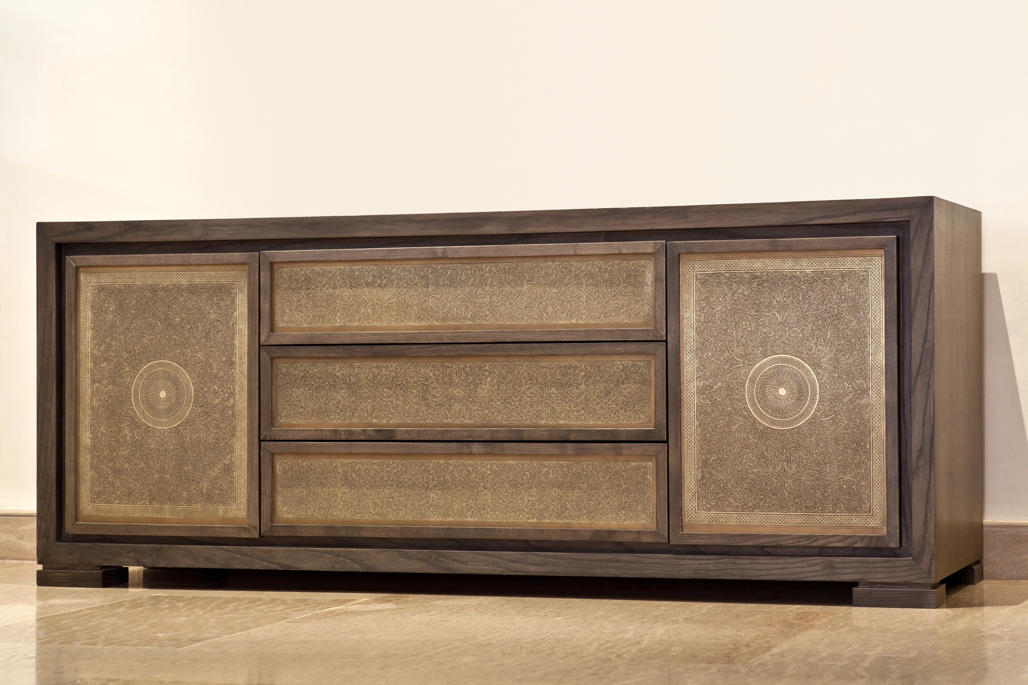 A wooden sideboard with patterned door panels and round medallion motifs, on a pale background.