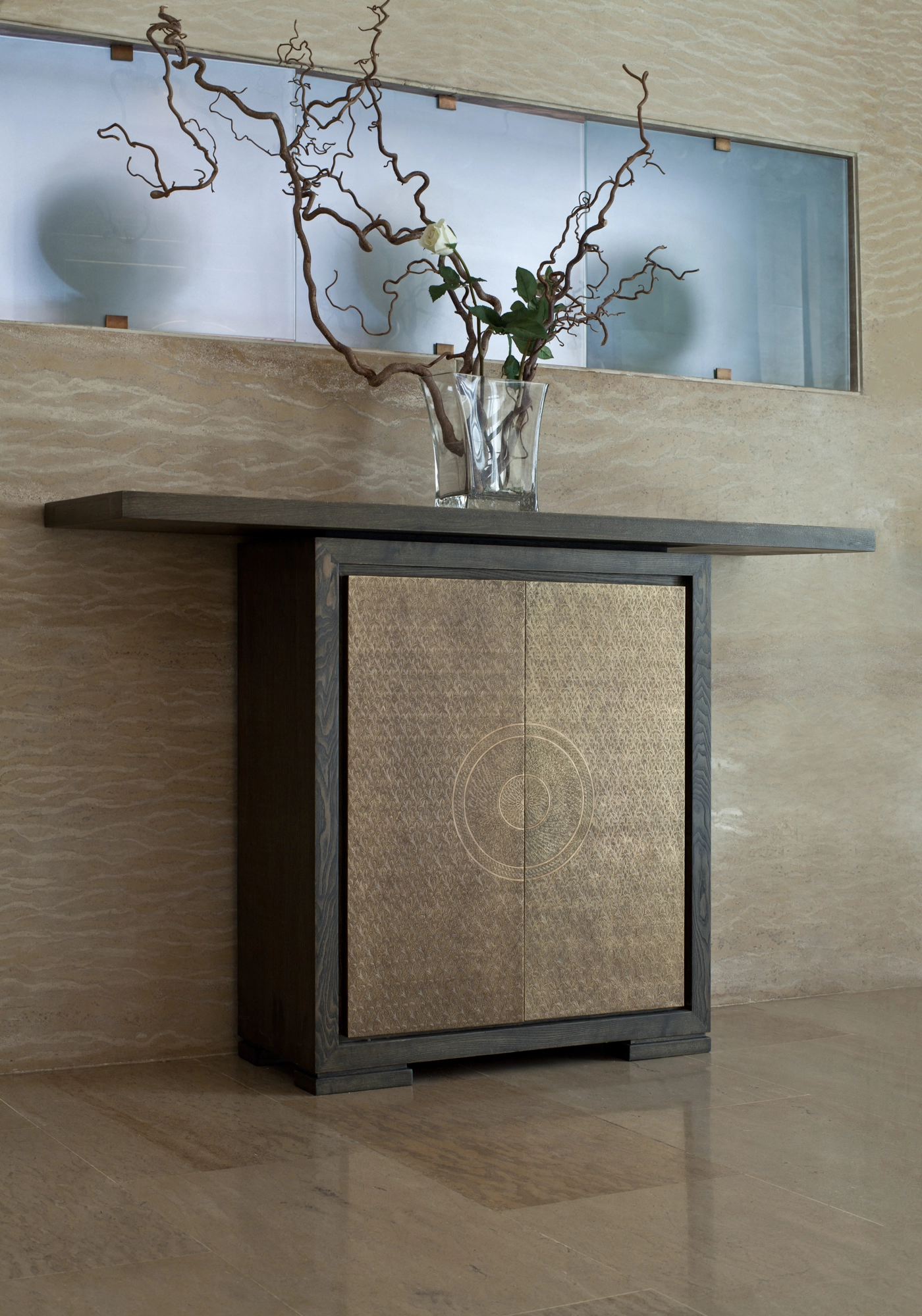 A cabinet with a woven-textured front, topped by a glass vase of bare branches, against a wall with a blue panel.