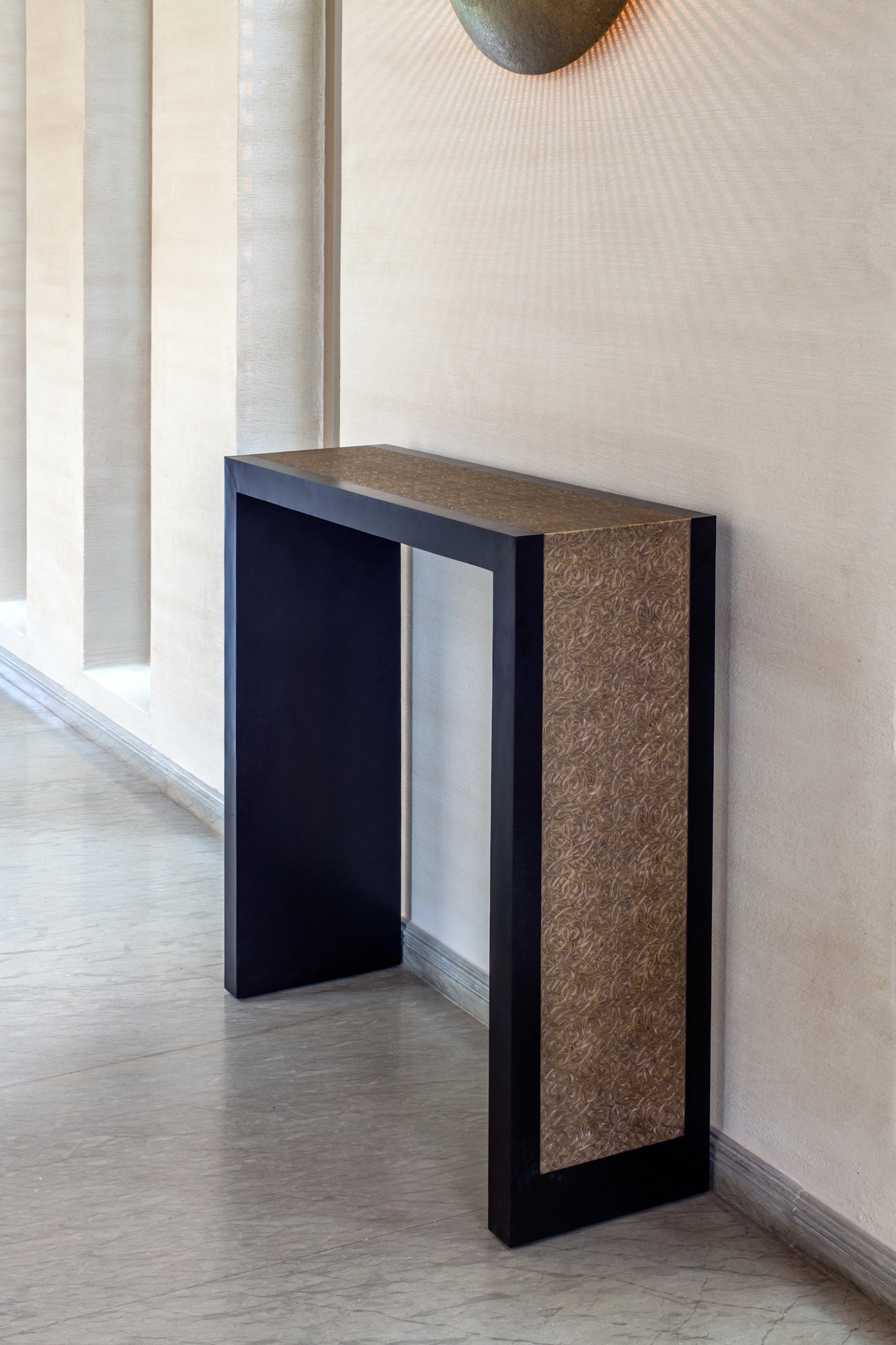 A console table with a dark frame and a pierced golden side panel, standing against a pale wall.
